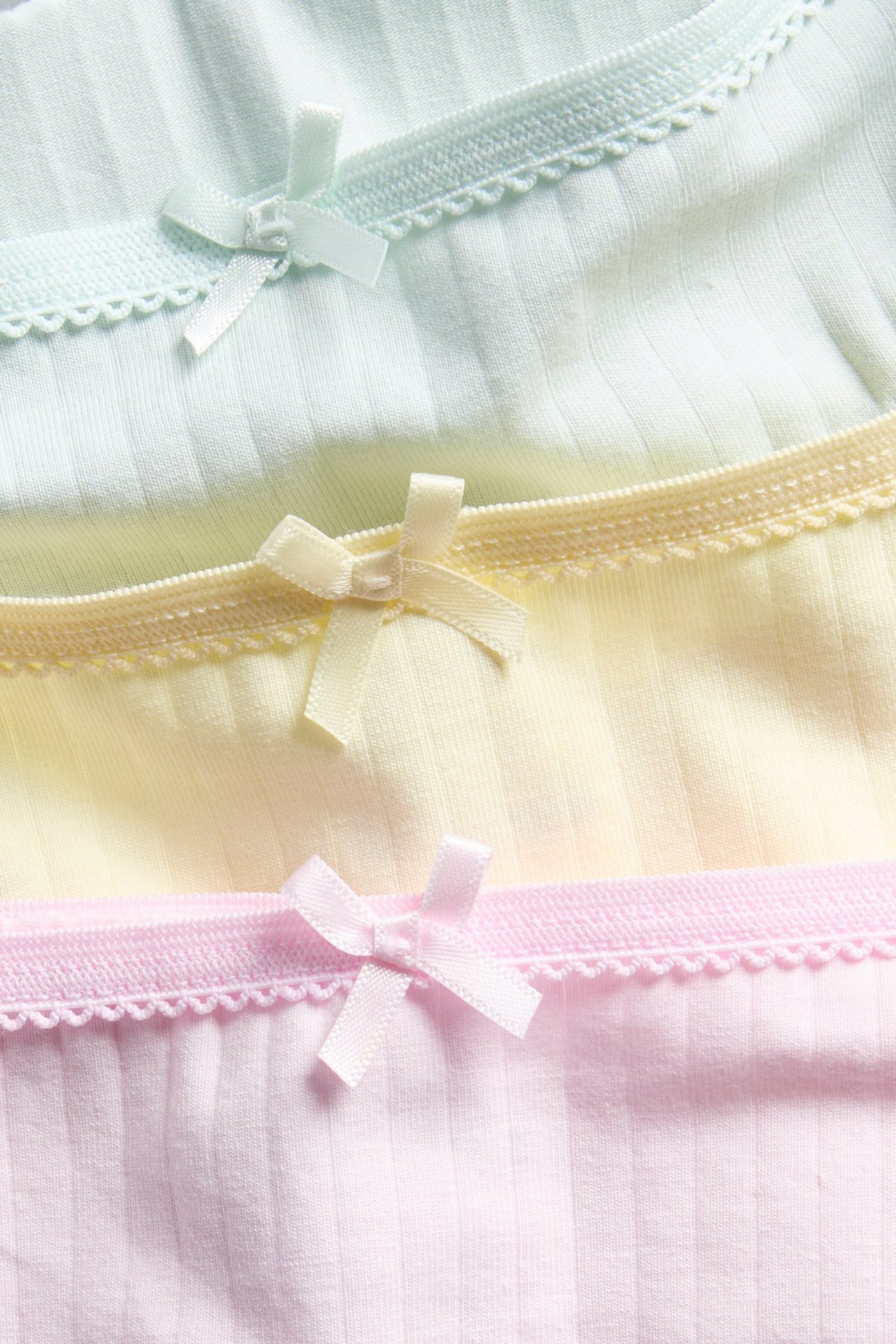 Lähikuva kolmesta ribatusta pikkuhoususta vaaleanpunaisena, keltaisena ja mintunvihreänä, picot-reunoilla ja ruseteilla.