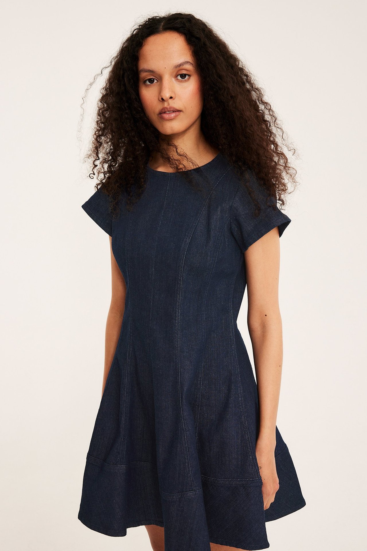 Edestä, nainen tummansinisessä A-linjaisessa farkkumekossa, lyhyillä hihoilla ja näkyvillä saumoilla.