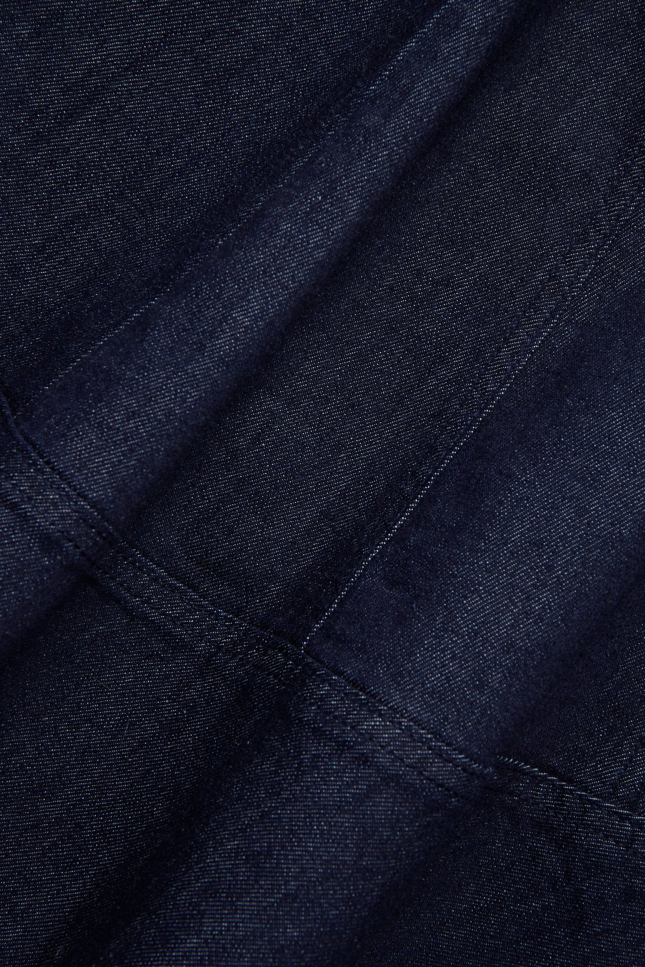 Lähikuva tummasta denimkankaasta ja A-linjaisen mekon näkyvistä saumoista.