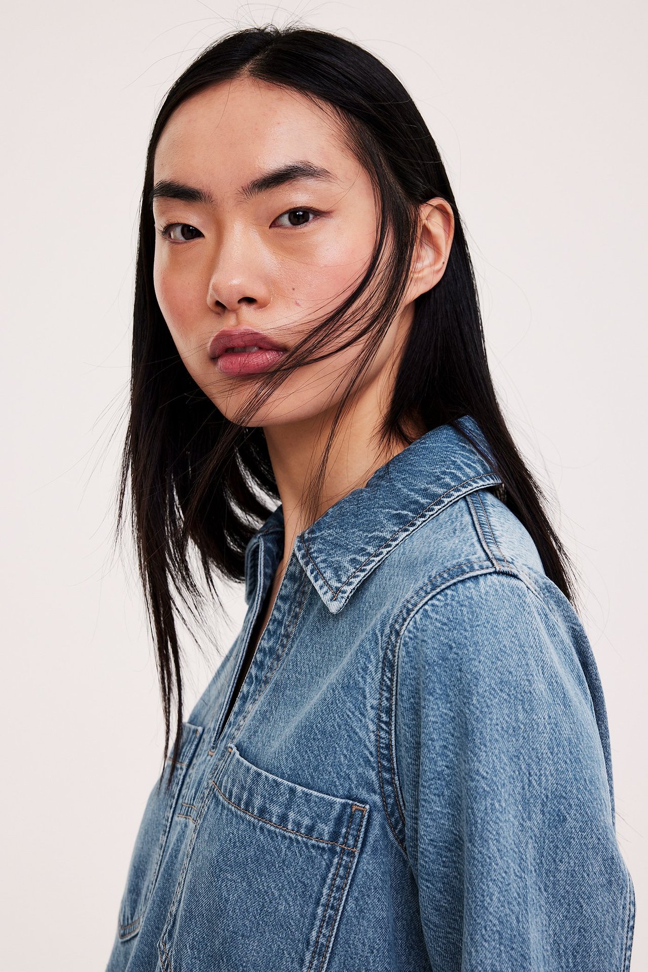 Nærbilde av kvinne i lyseblå dongerikjole med krage og brystlomme.