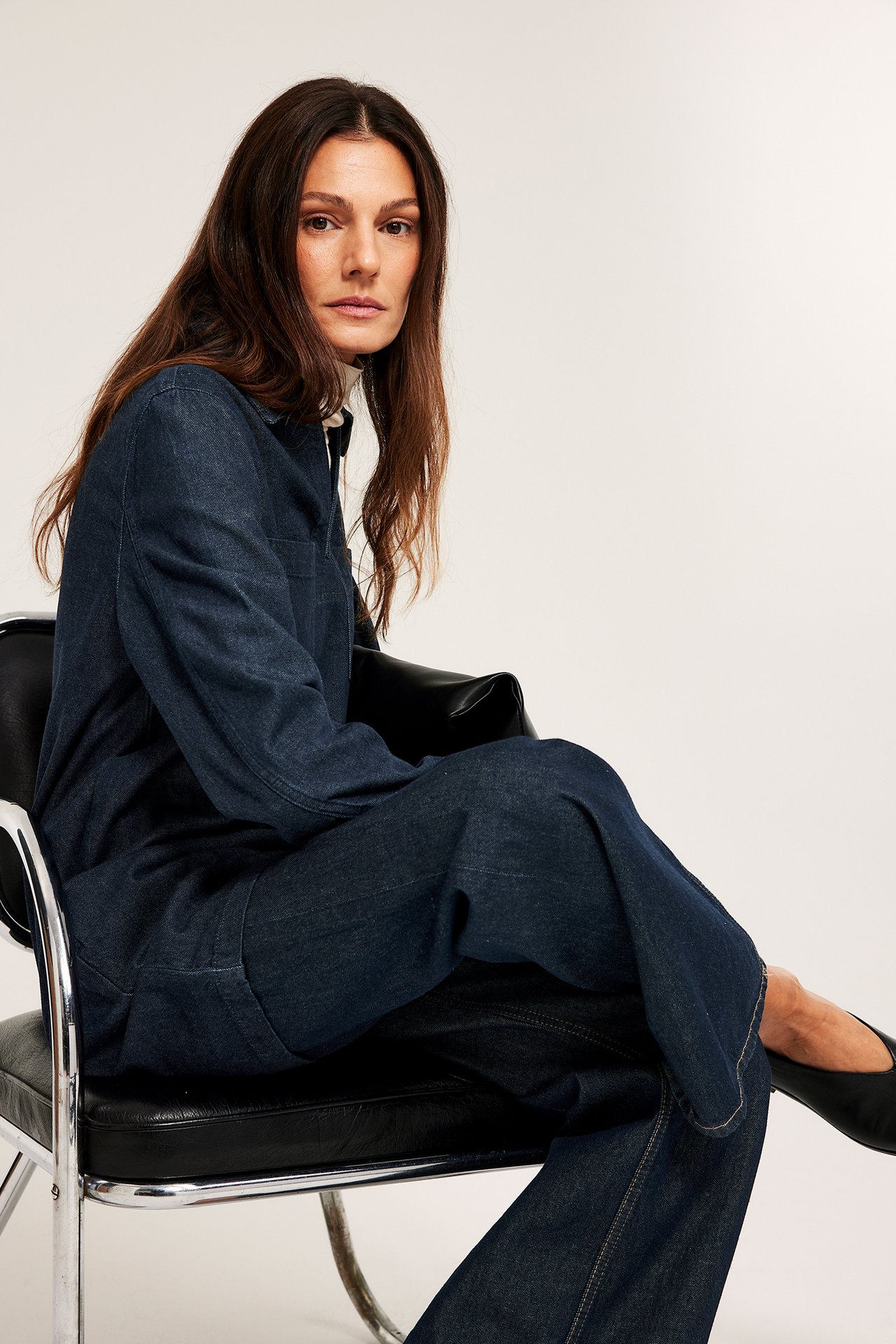 Kobieta w ciemnoniebieskiej dżinsowej sukience z kołnierzem i kieszeniami na piersi, na białym golfie, widok z przodu.