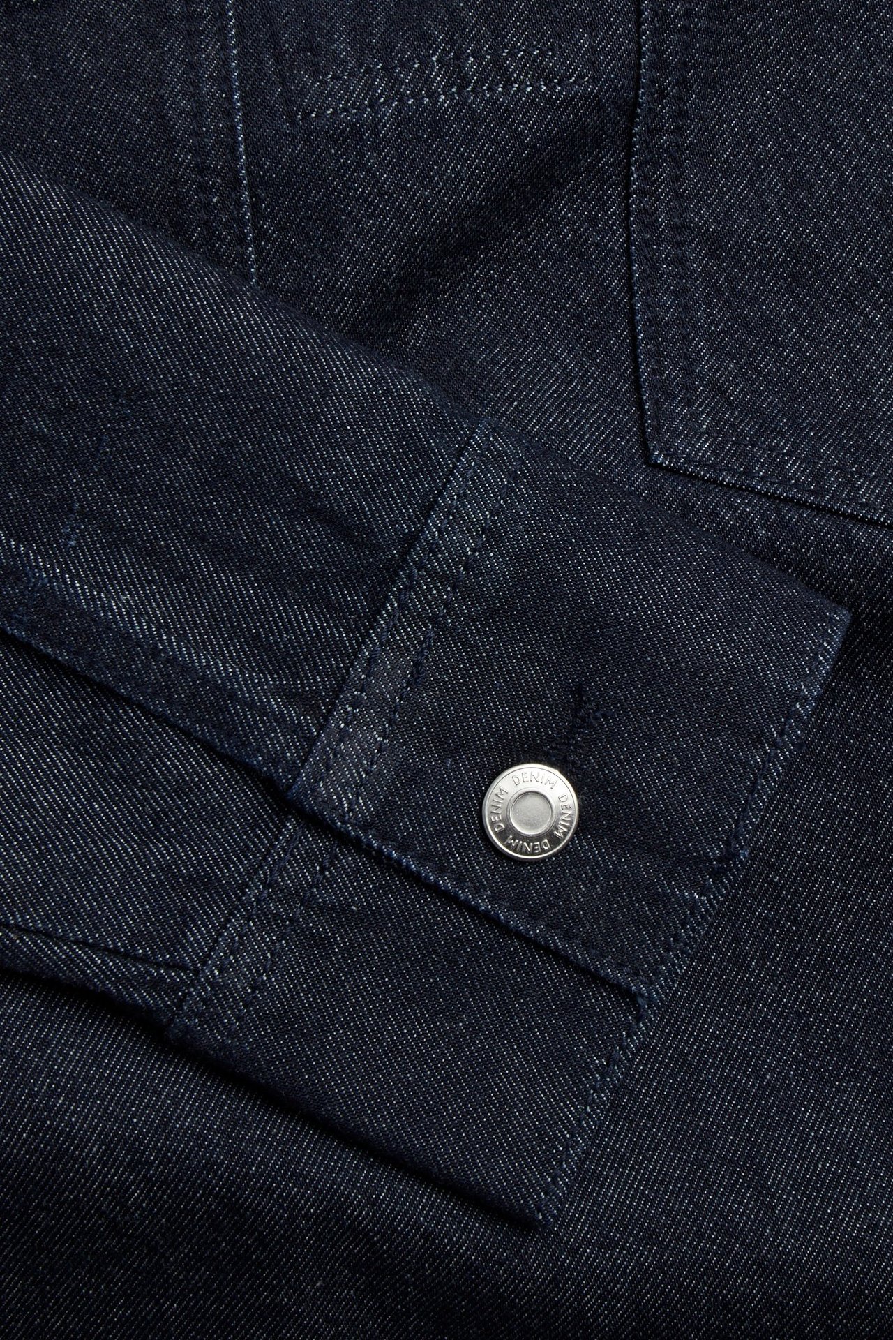 Lähikuva tummansinisen denim-mekon hihansuusta ja hopeisesta napista.