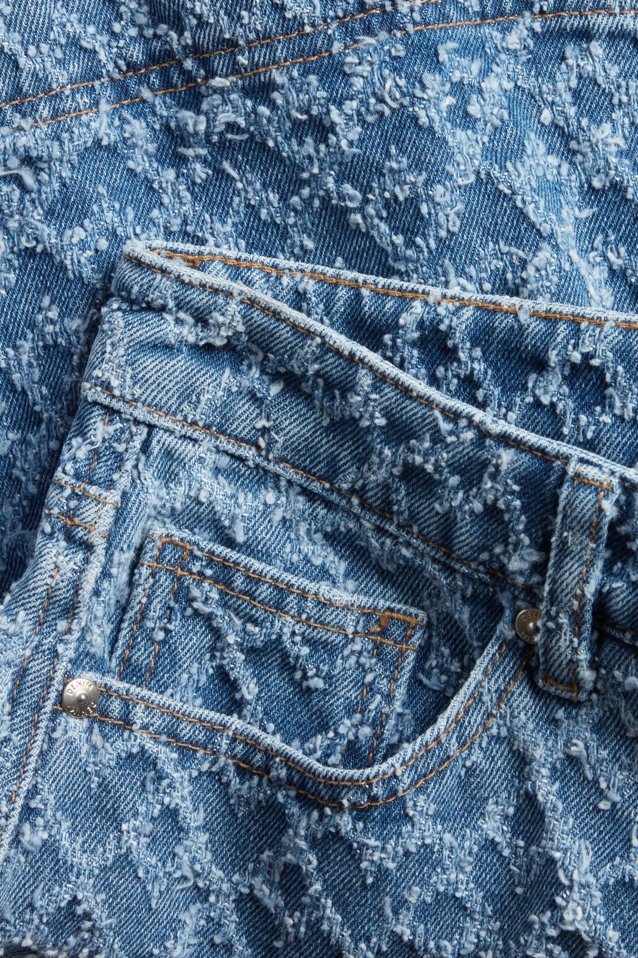 Zbliżenie niebieskiej dżinsowej minispódniczki ze strukturalnym wzorem w serca i kontrastowymi szwami na kieszeniach.