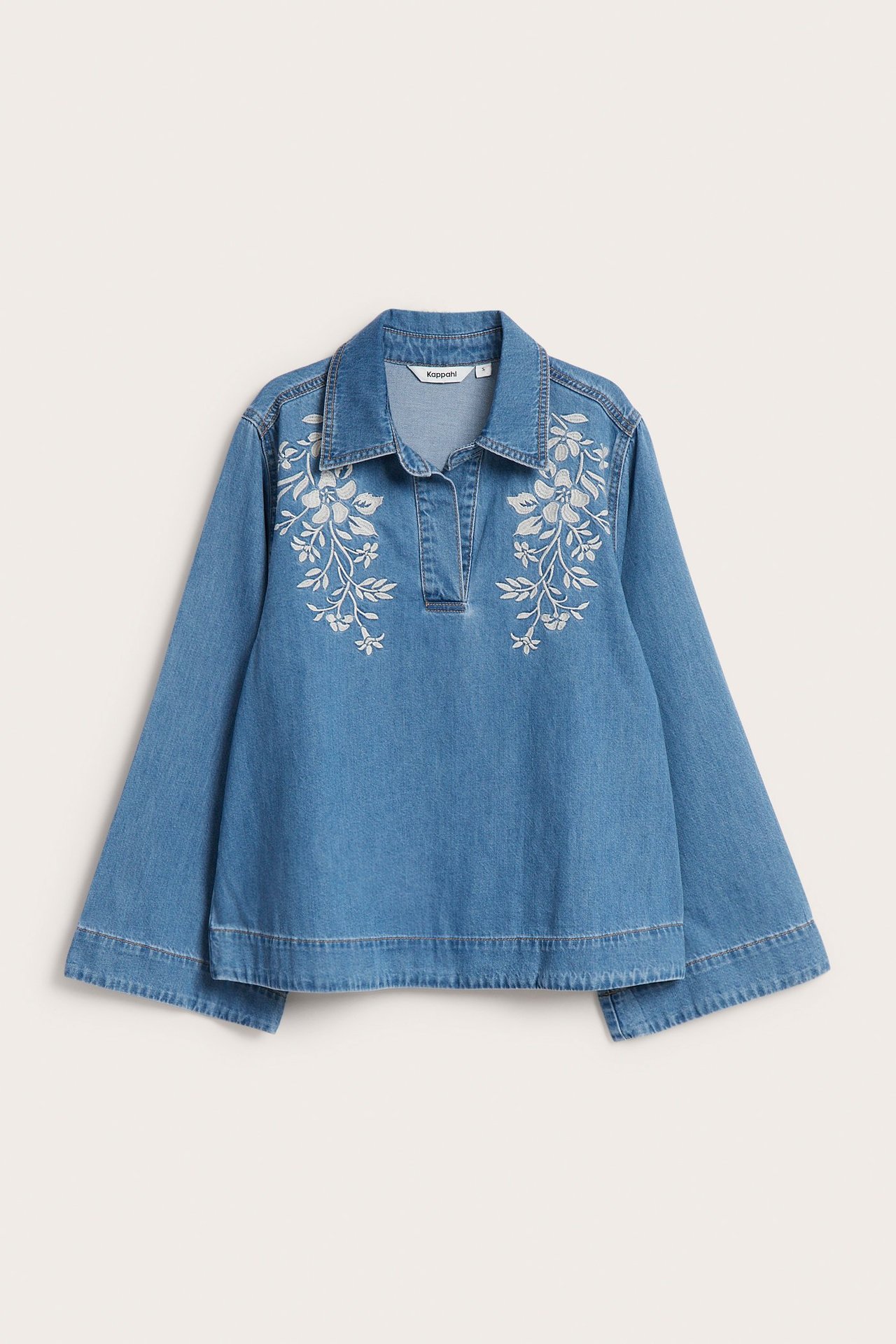 Edestä: Sininen denim-paitapusero, valkoinen kukkakirjonta rinnassa ja leveät hihat.