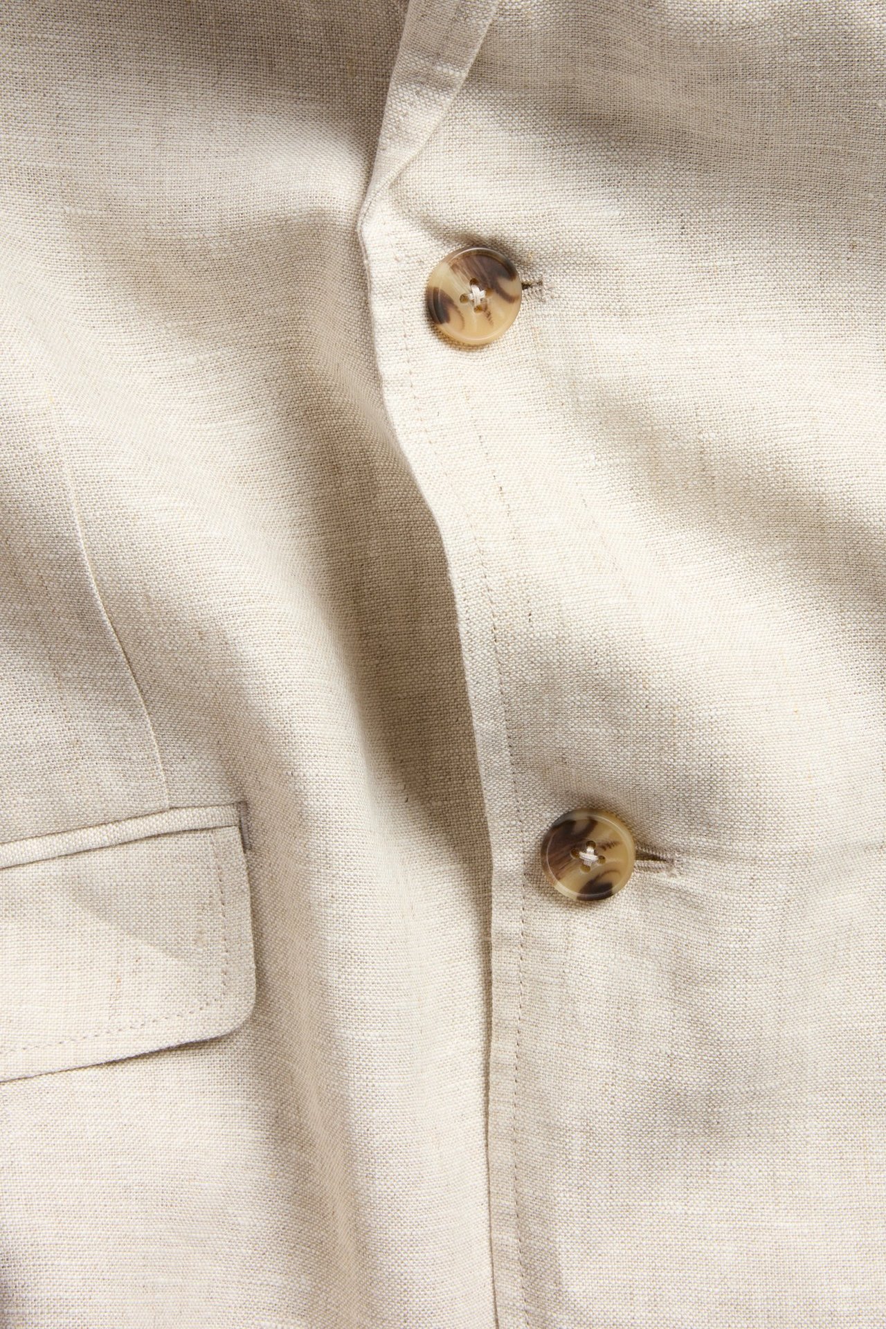 Nærbilde av menns beige linneblazer i regular fit, med to brune knapper og en klafflomme.