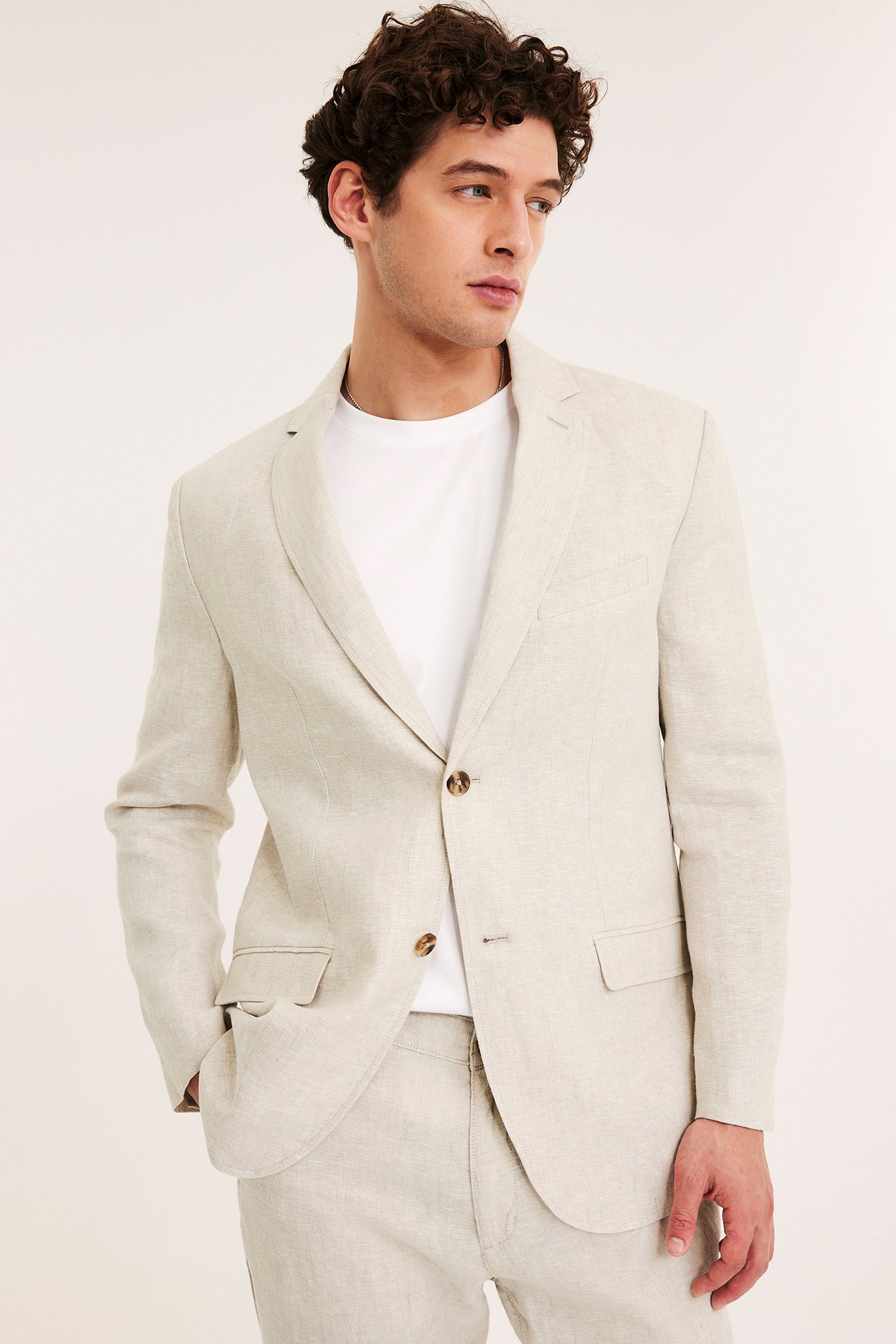 Frontbilde av en mann i en beige regular fit linblazer, en hvit t-skjorte og matchende linbukser.