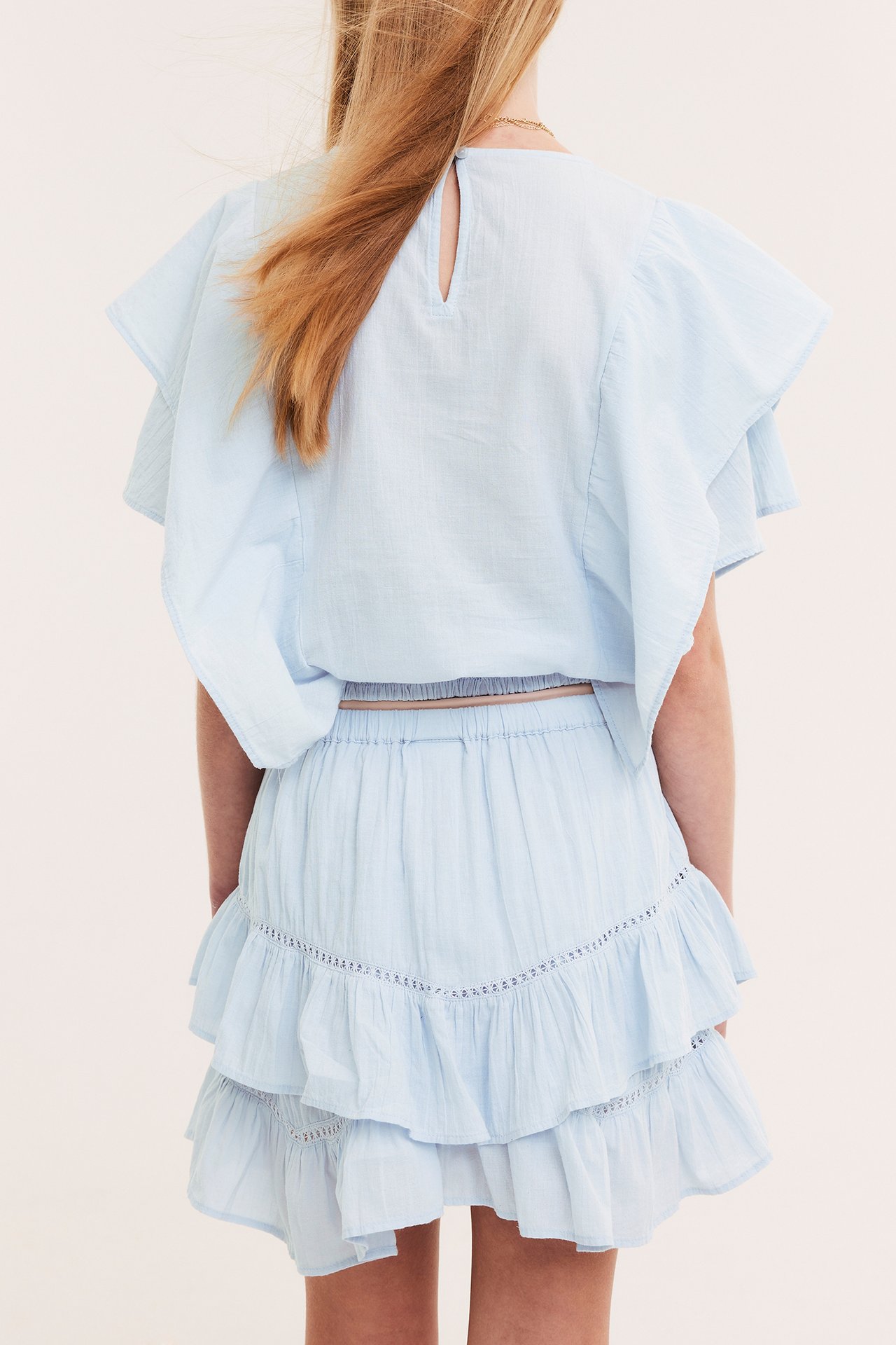 Lapsen takaa: vaaleansininen pitsikoristeinen röyhelöhame kuminauhavyötäröllä ja röyhelötoppi.