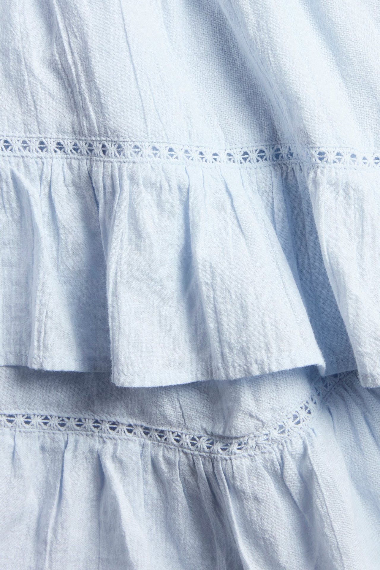 Närbild av en ljusblå volangkjol med spetsdetaljer i flera lager.