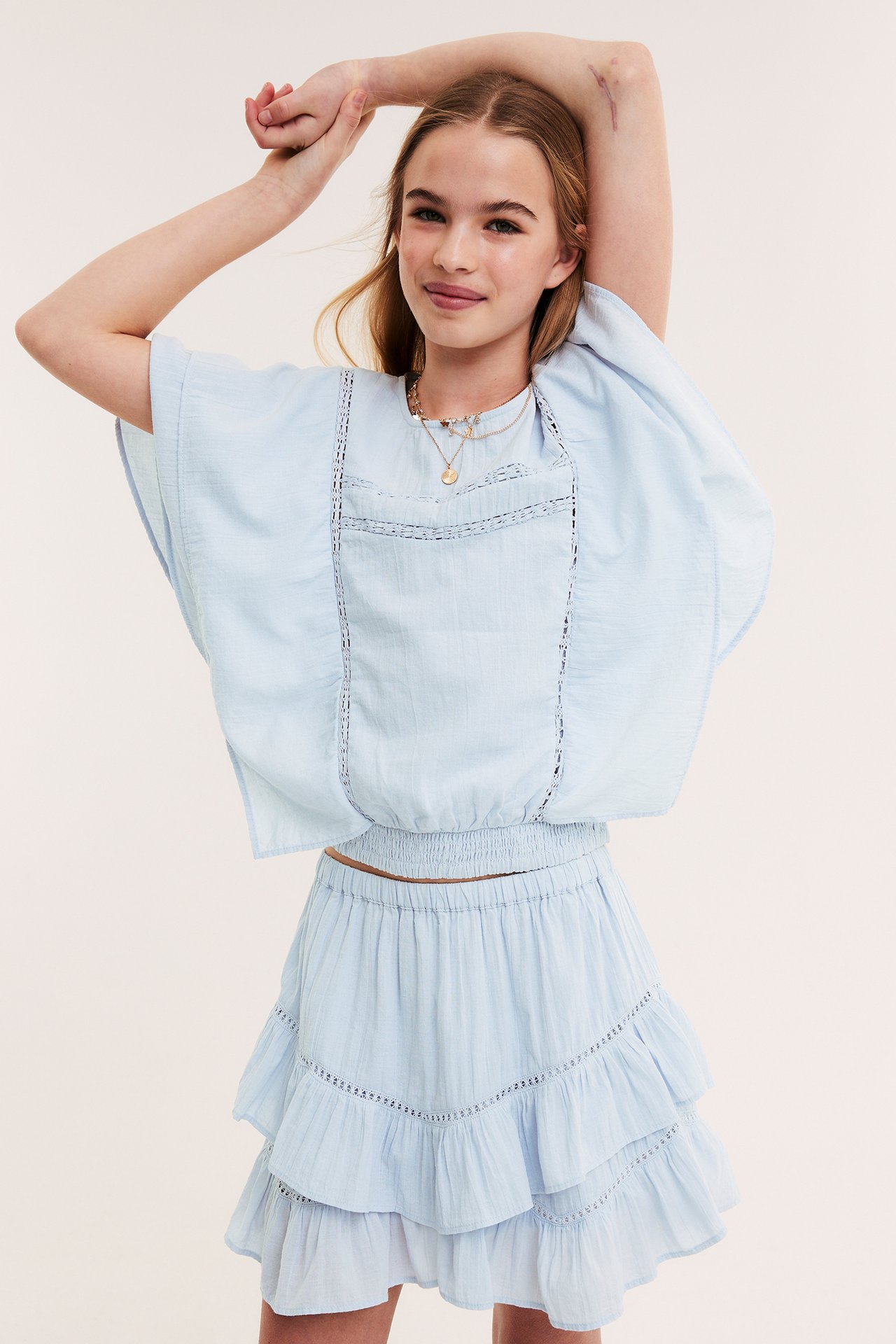 Framifrån: Barn i ljusblå volangkjol med resår, matchande topp med spets och halsband.