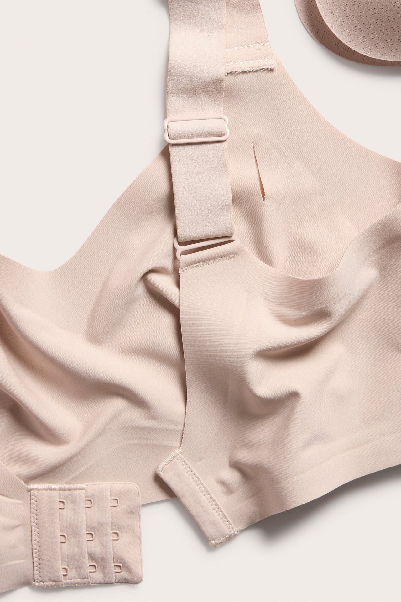 Nærbilde av en lys rosa bøyleløs mikro-bh med justerbar bred stropp, krok-og-malje-lukking og avtagbar vattering.