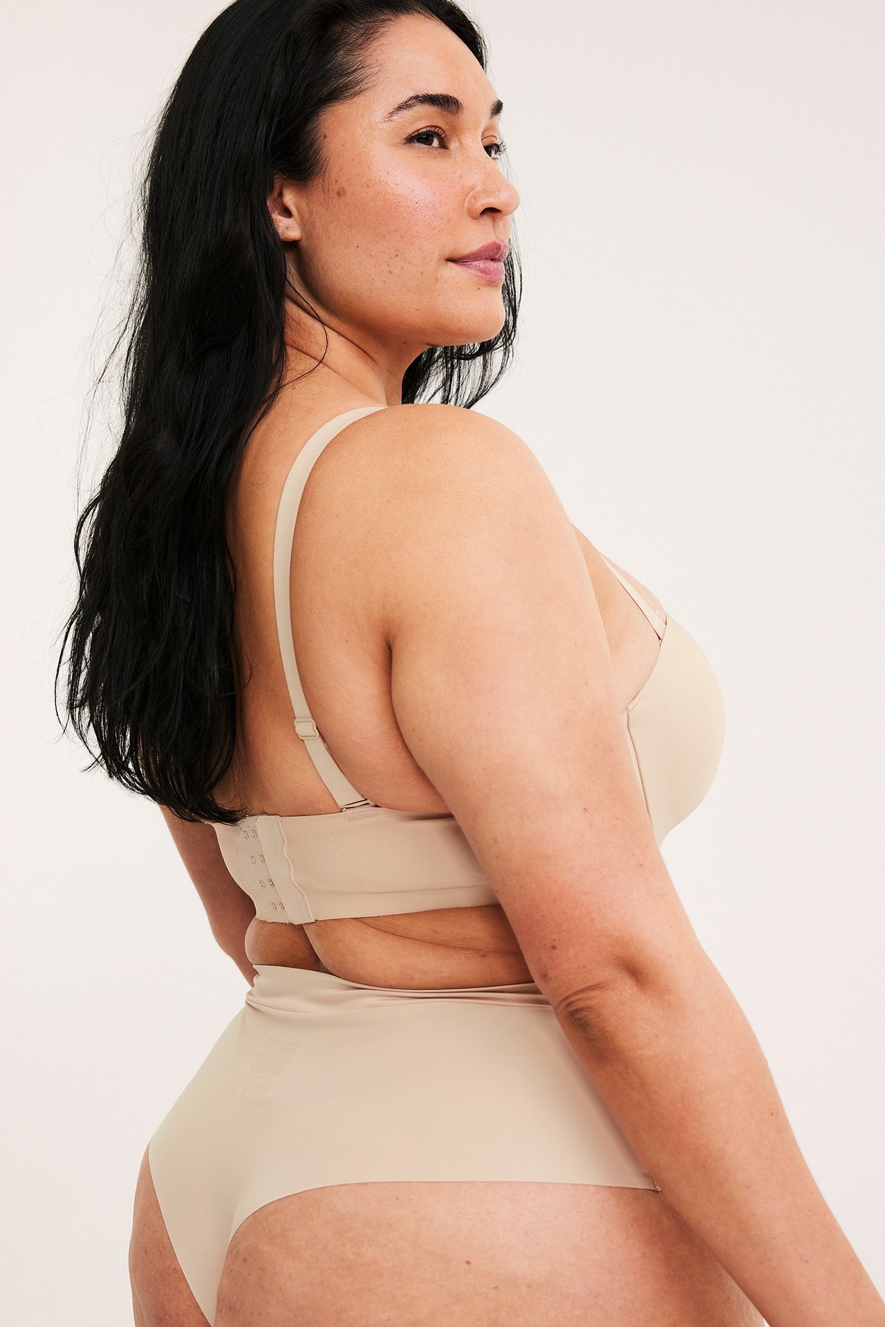 Sida vy av en kvinna som bär en ljusbeige sömlös micro stringtrosa med matchande BH.