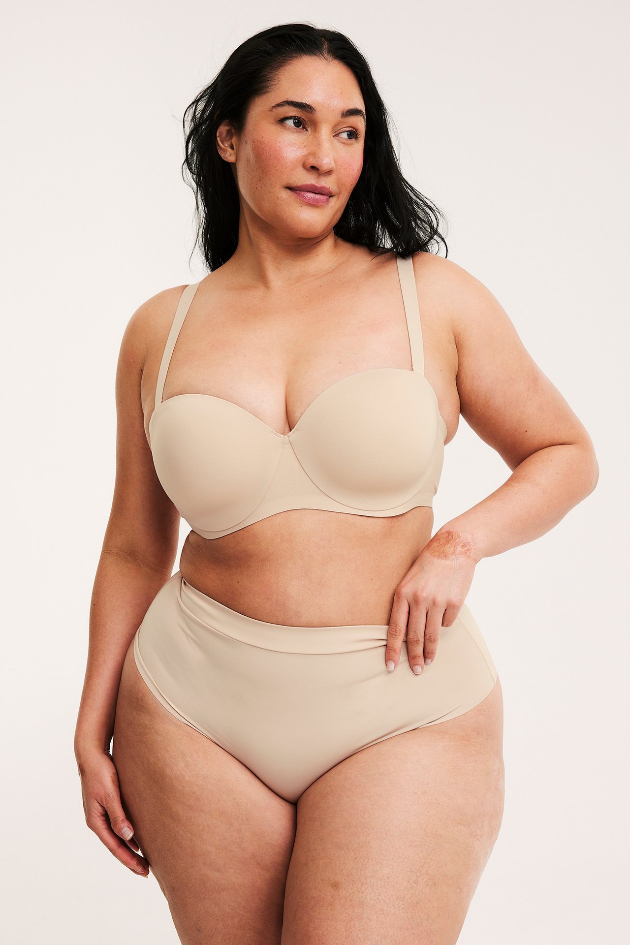 Framifrån: Kvinna i ljusbeige hög midja trosa med resårlinning och matchande axelbandslös BH.
