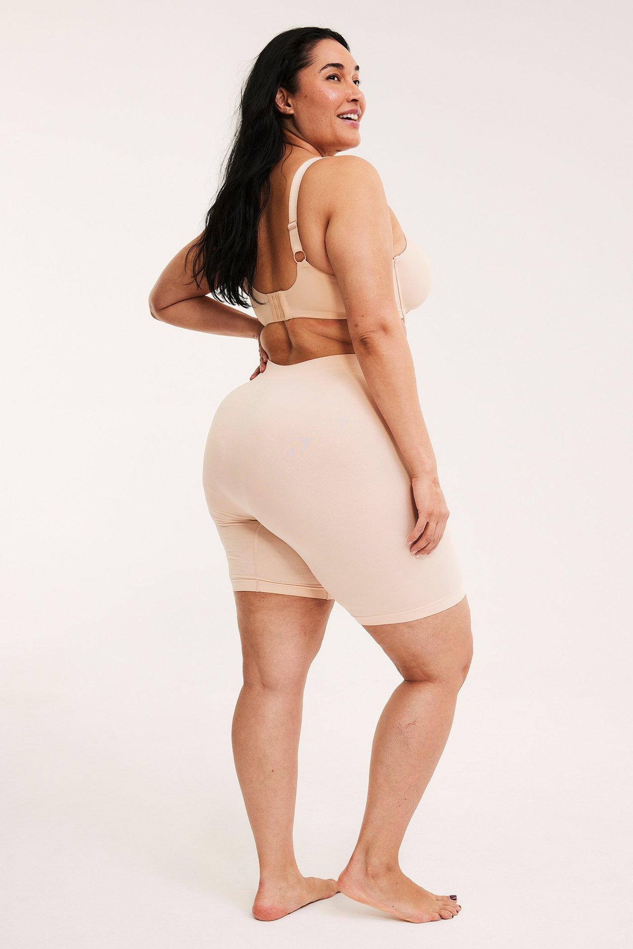 Sida bakifrån av kvinna i ljusrosa sömlösa högmidjade shorts och matchande bh.