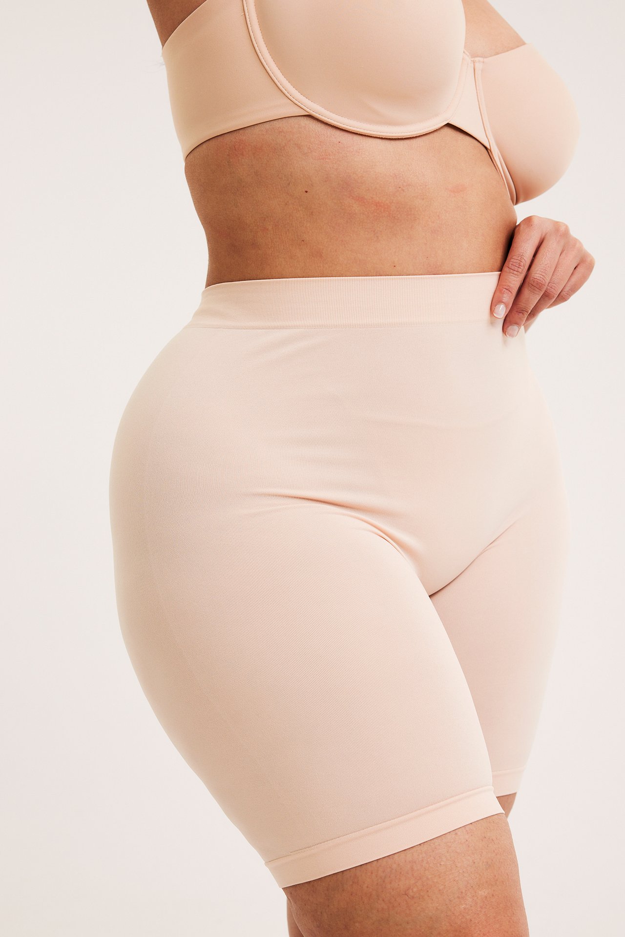 Naisen sivukuva yllään vaaleanpunaiset saumattomat korkeavyötäröiset shortsit ja yhteensopivat rintaliivit.