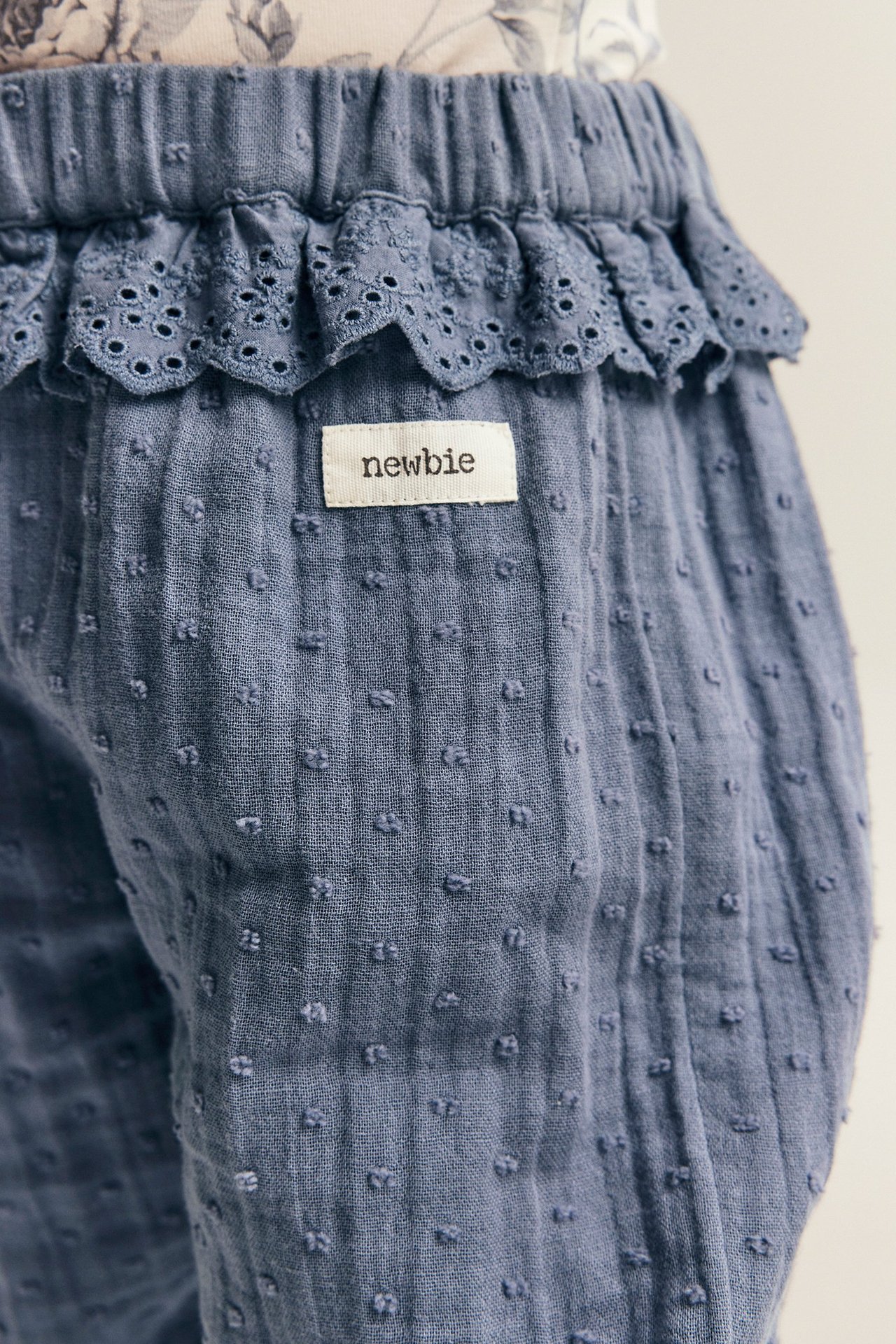 Zbliżenie na niebieskie, teksturowane bawełniane spodnie niemowlęce z koronkową falbaną i gumkami.