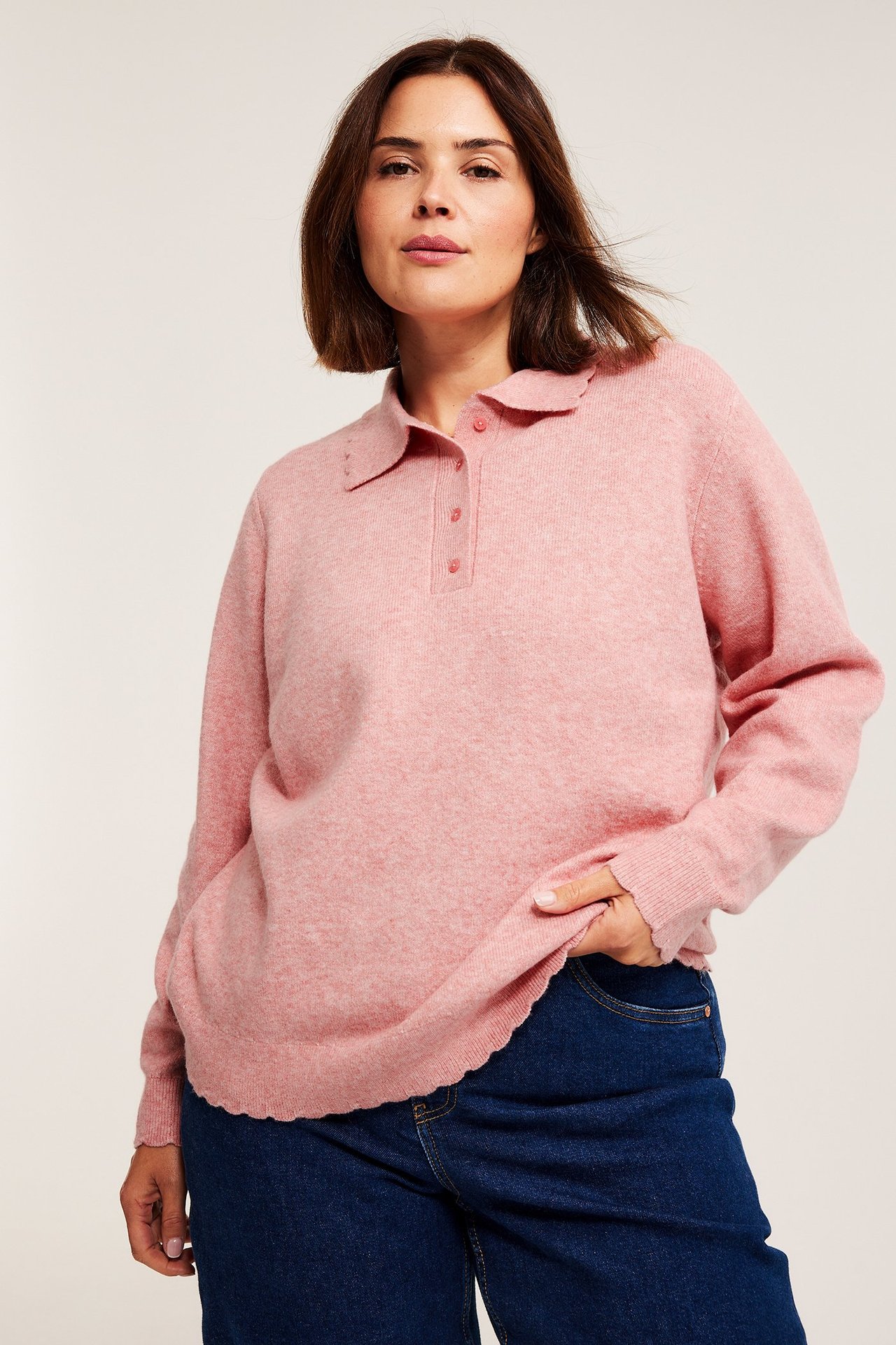 Frontbilde: kvinne i rosa melert finstrikket polo-genser med bølgete kanter og mørkeblå jeans.