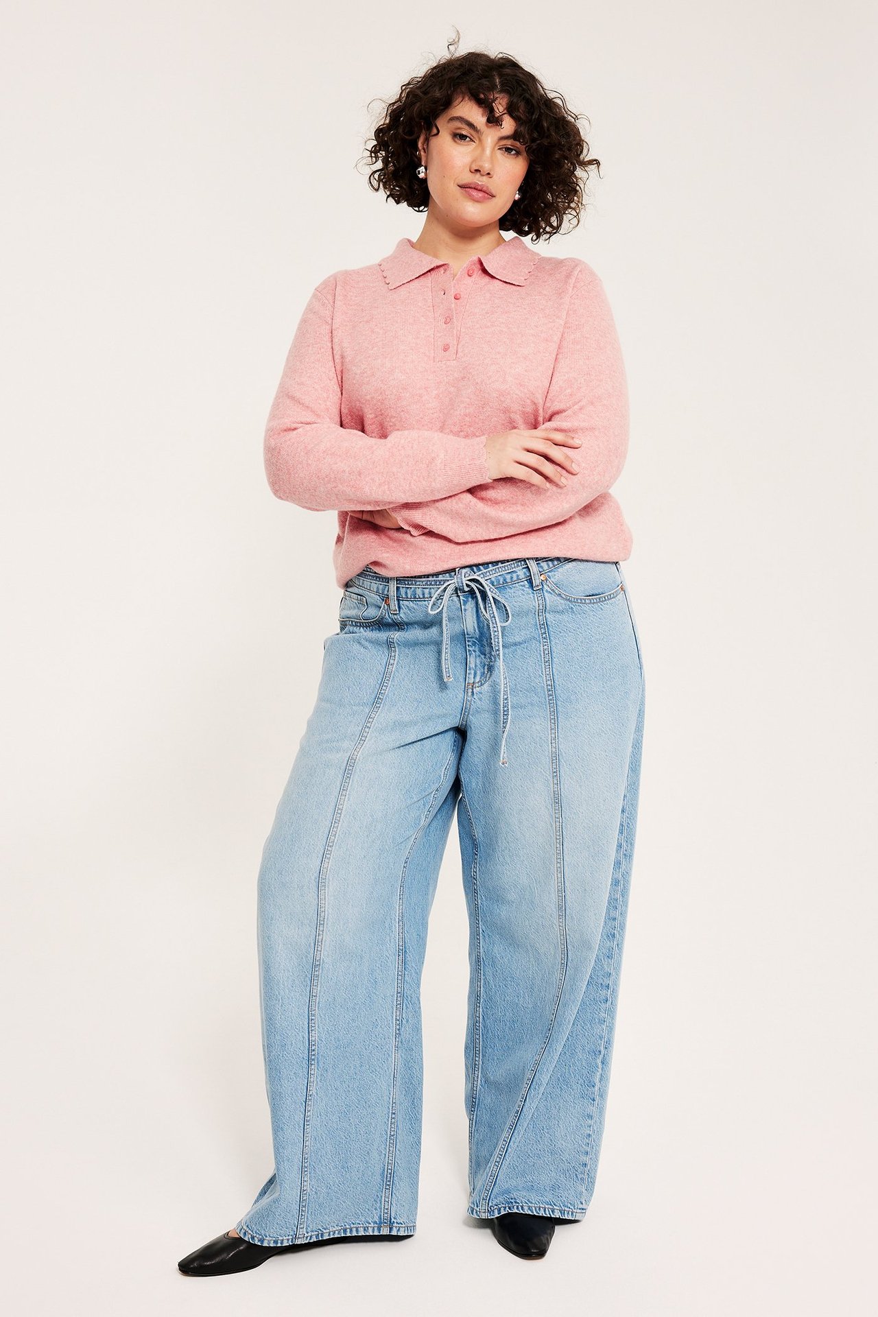 Frontbilde: Kvinne i rosa melert finstrikket pikégenser, lyseblå jeans og svarte flate sko.