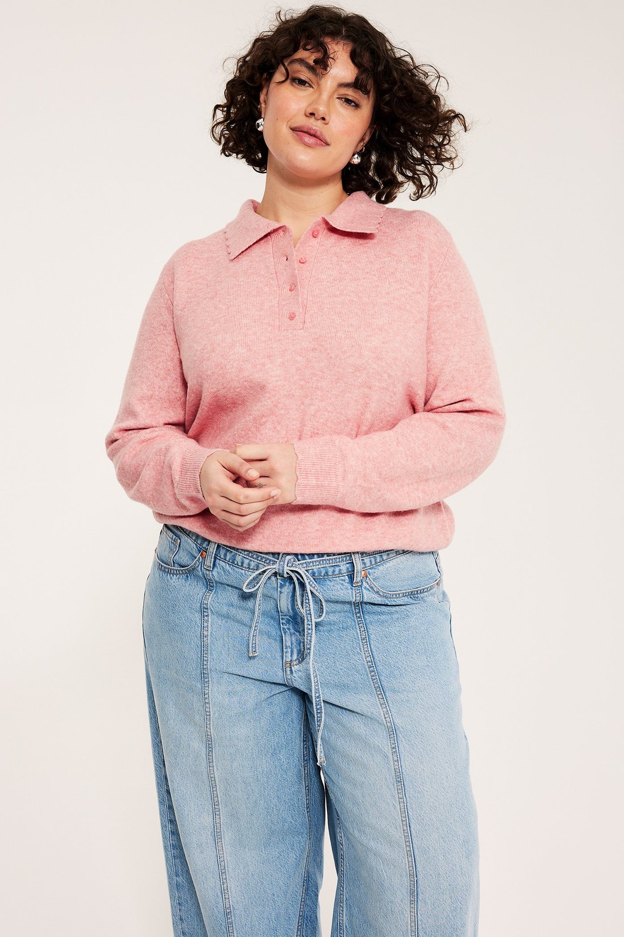 Forfra: Kvinne i rosa melert finstrikket genser med bølget krage og lysblå vide jeans.