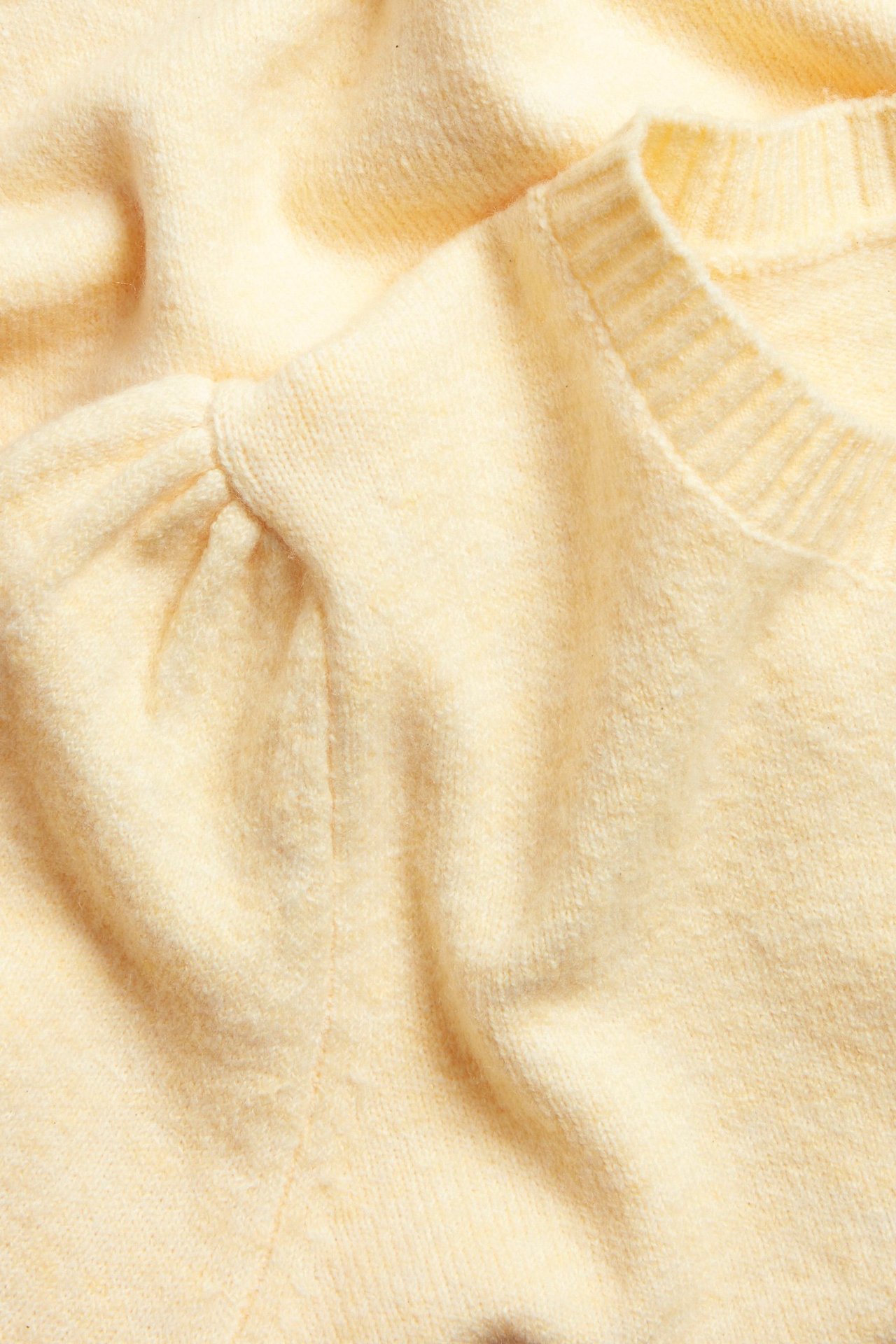 Zbliżenie na jasnopudrowy melanżowy kardigan z krótkim bufiastym rękawem i okrągłym dekoltem.