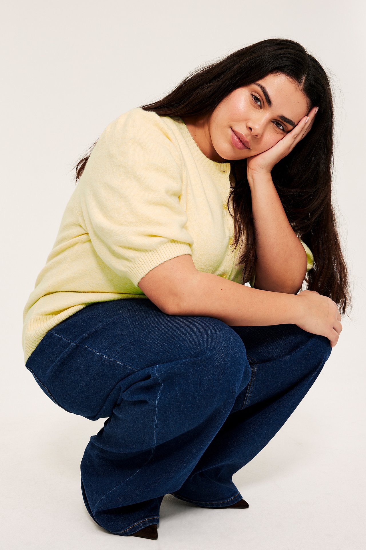 Kobieta w jasnym, żółtym melanżowym kardiganie z krótkimi bufiastymi rękawami i ciemnoniebieskich jeansach.