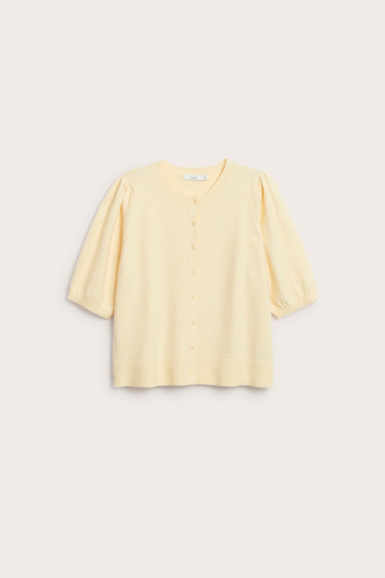 Edestä, vaaleankeltainen meleerattu lyhythihainen neuletakki pussihihoilla, pyöreällä pääntiellä ja napeilla edessä.