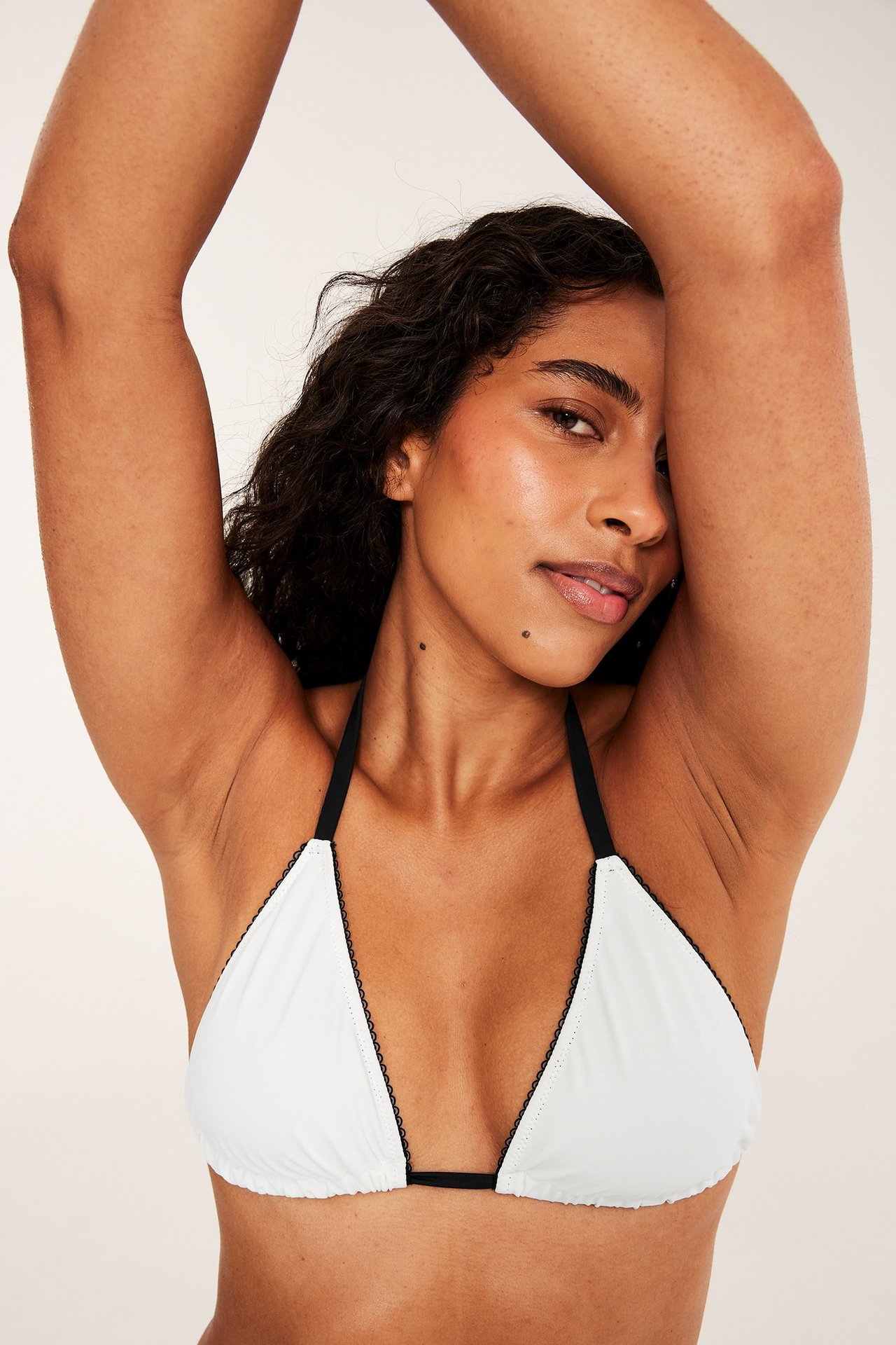 Nærbilde forfra av en kvinne i en offwhite vattert trekantbikini-BH med svarte picotdetaljer.