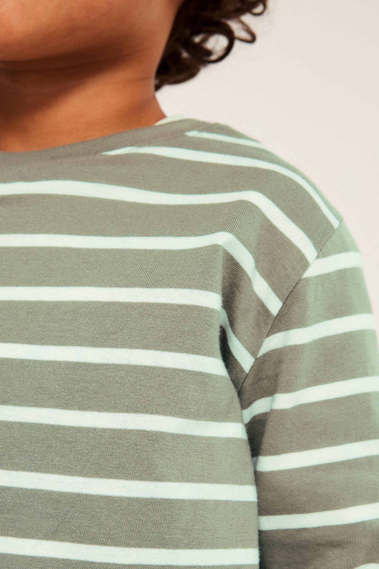 Närbild av ett barn som bär en mörkgrön långärmad bomulls t-shirt med ljusgröna ränder.