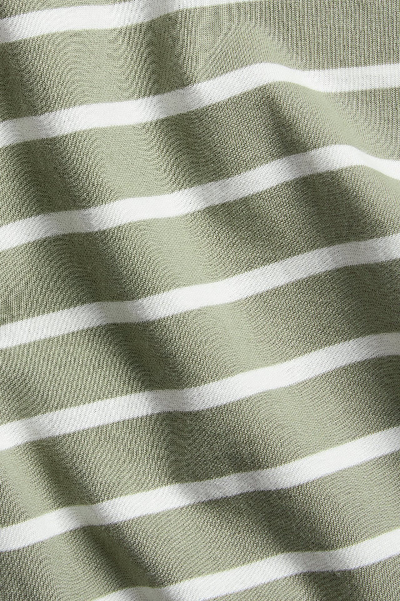Zbliżenie na ciemnozielono-biały bawełniany materiał w paski, na koszulkę z długim rękawem.