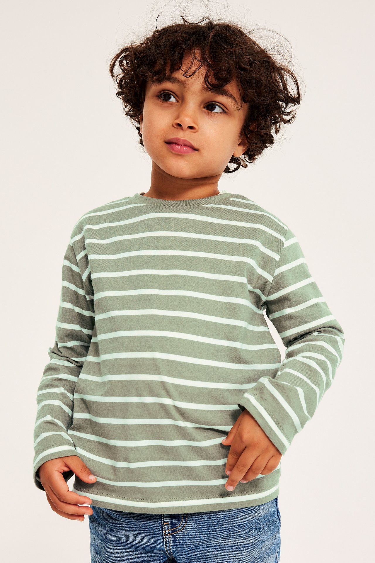 Framsida av ett barn i en mörkgrön och ljusgrön randig långärmad bomulls-t-shirt och blå jeans.