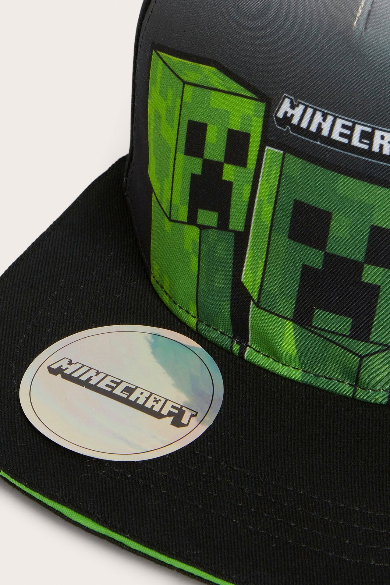 Närbild framifrån på en svart flat cap med grönt Minecraft Creeper-tryck.