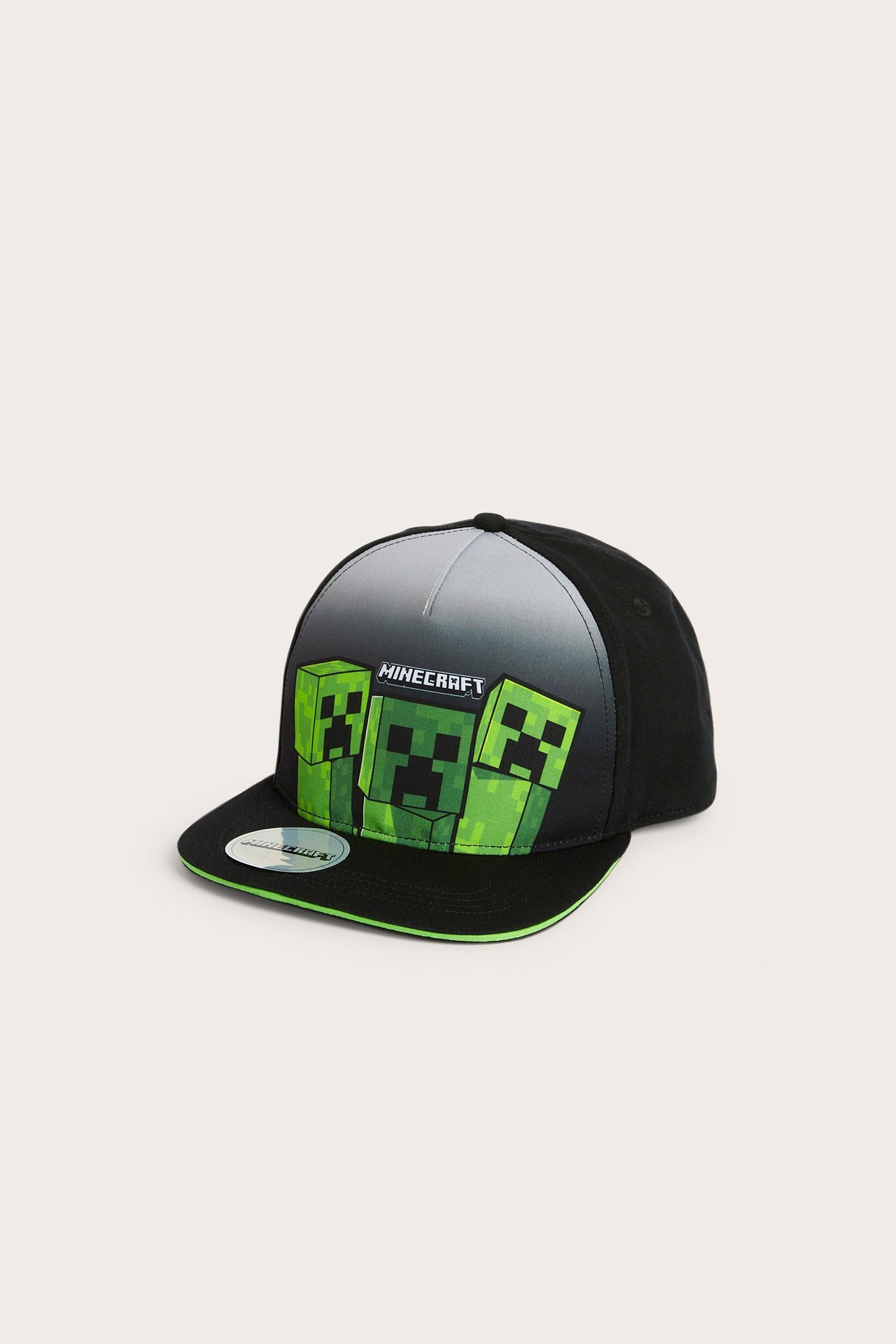 Framsida av en svart flat keps med grönt Minecraft Creeper-tryck och logga framtill.