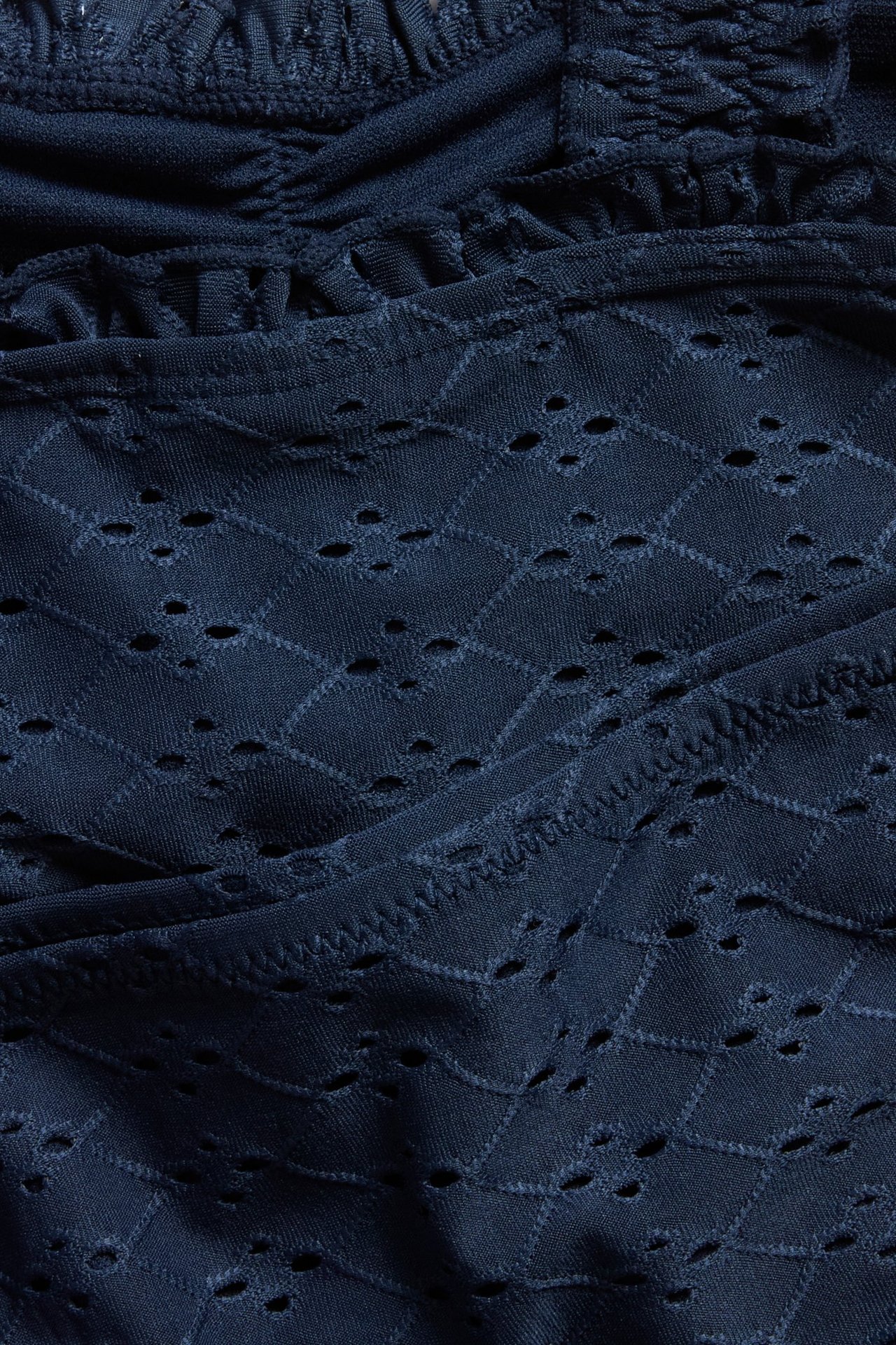 Lähikuva laivastonsinisestä bikinista, jossa on broderie anglaise -kuvio ja rypytyksiä.