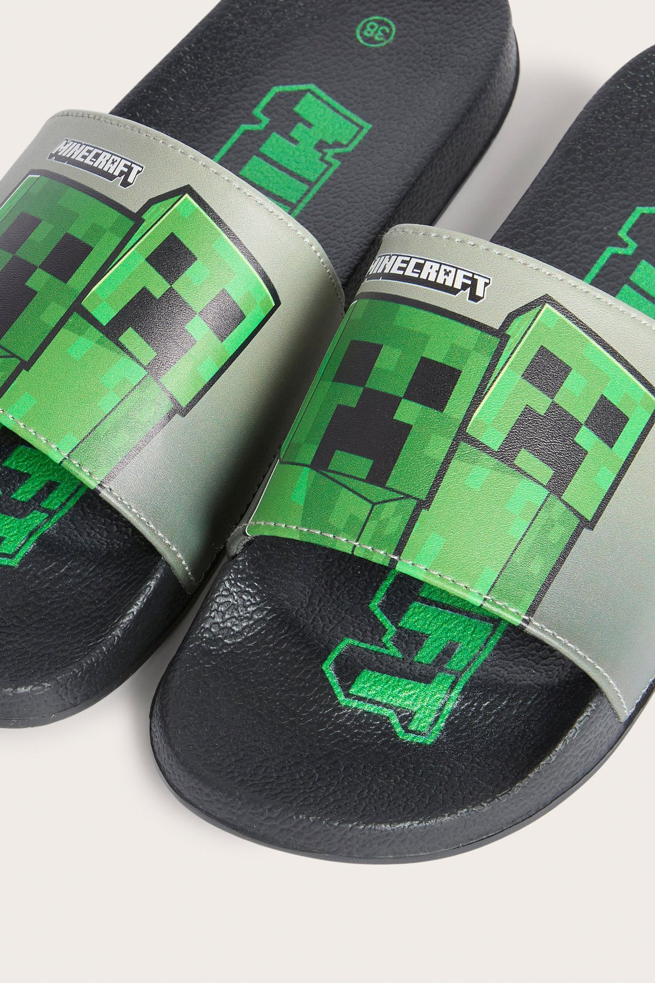 Zbliżenie z góry na czarne klapki dziecięce z szarymi paskami i zielonym nadrukiem Minecraft Creeper.