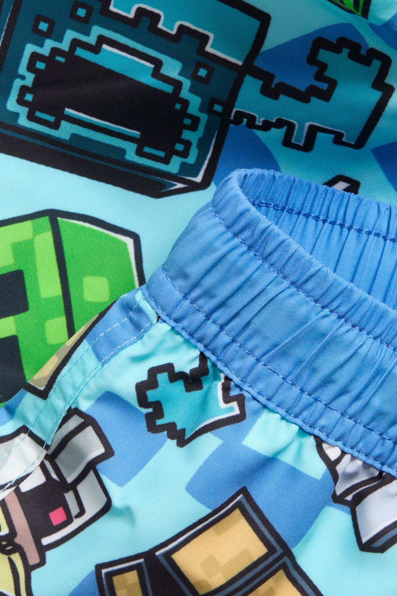 Lähikuva sinisistä kuvioiduista Minecraft-uimahousuista, joissa elastinen kiristysnyörillinen vyötärö.