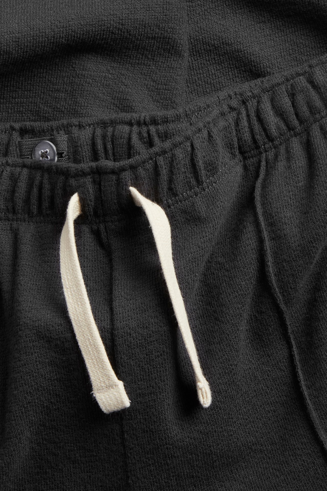 Närbild framifrån av svarta texturerade bomullsjoggingbyxor med resårmidja och ljus falsk dragsko.