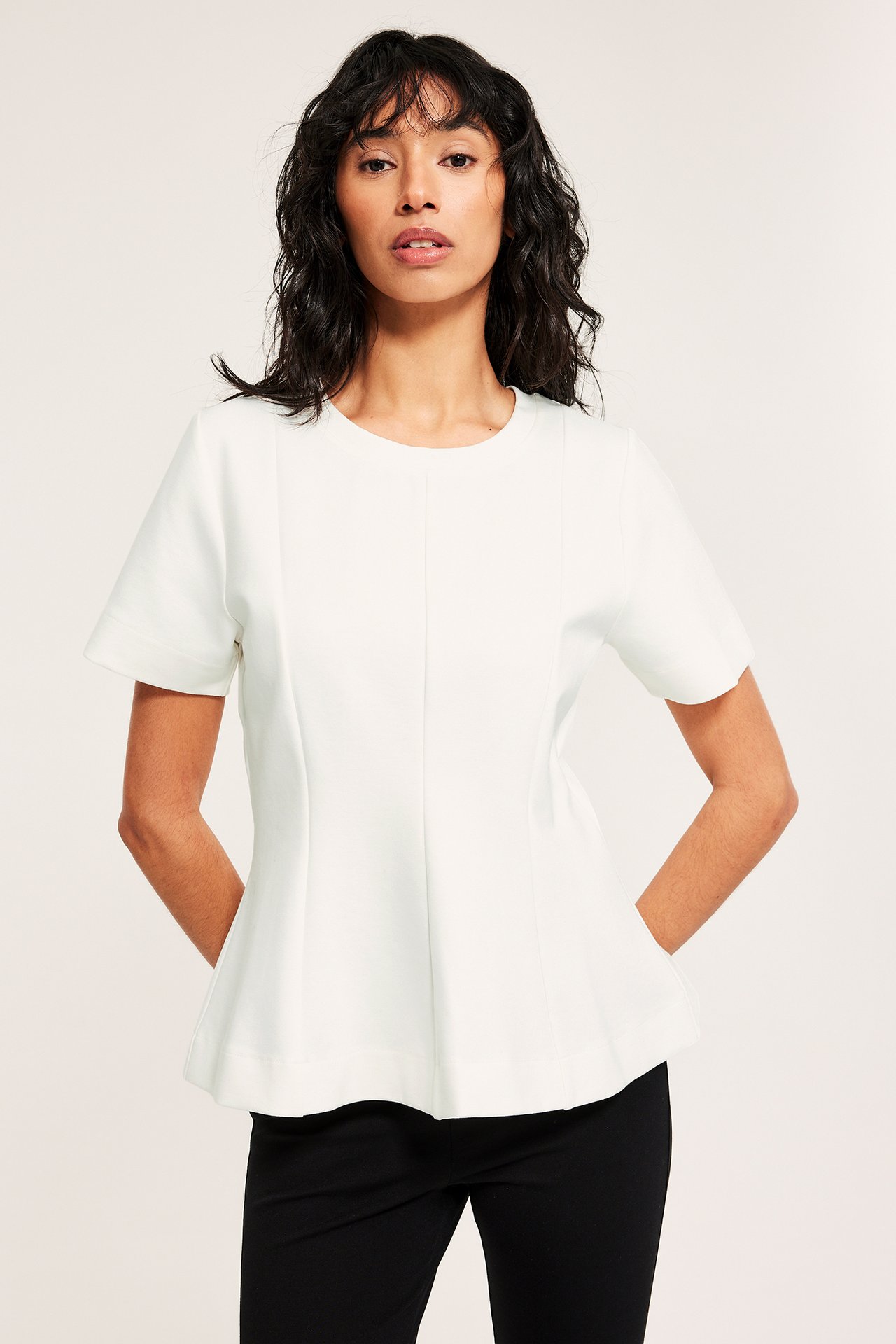 Frontbilde av en kvinne i en offwhite kortermet peplumtopp og svarte bukser.