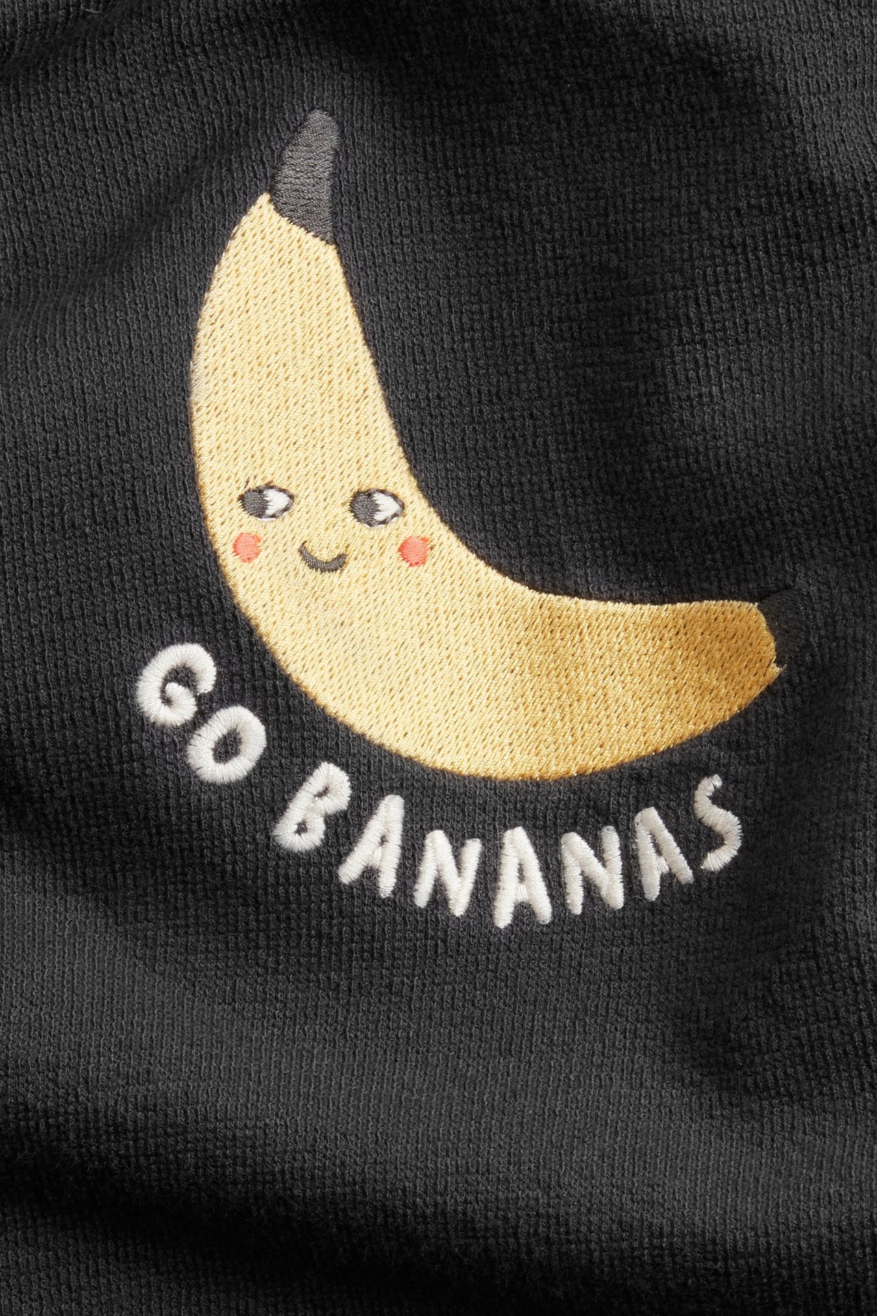 Närbild på en svart bomullssweatshirt med gul bananbrodyr och texten "GO BANANAS".