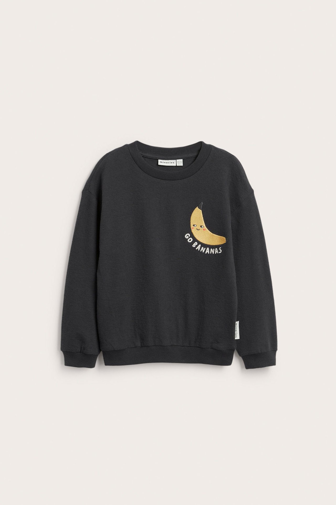 Framifrån: en svart barnsweatshirt i texturerad bomull med ett broderat gult banantryck.