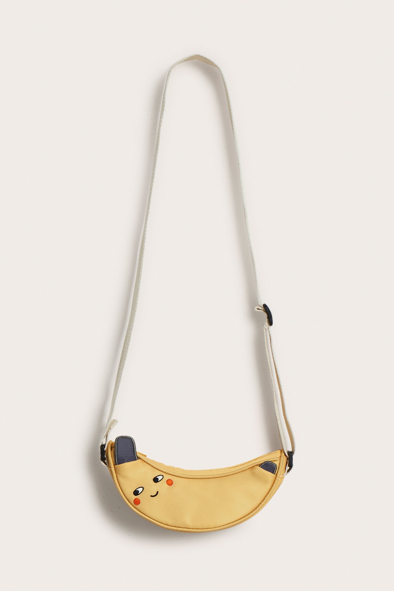 Widok z przodu żółtej torebki-banana dla dzieci z haftowaną buzią i regulowanym paskiem.