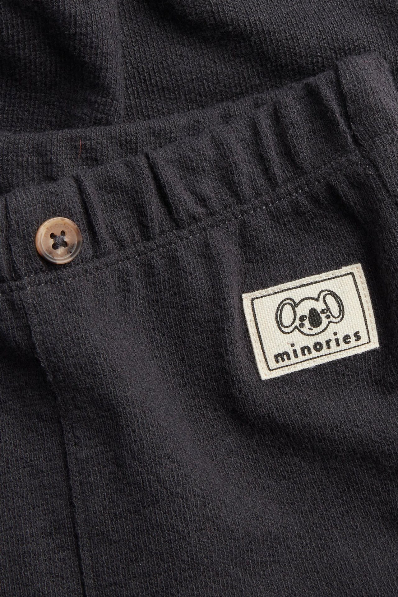 Lähikuva tummanharmaista yksivärisistä vauvan collegehousuista, resori vyötäröllä, valenappi, logopaikka.