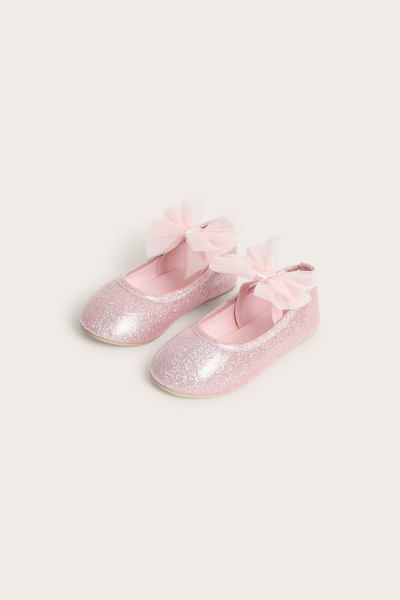Widok z przodu dwóch jasnoróżowych brokatowych balerinek z siateczkowymi kokardkami na piętach.