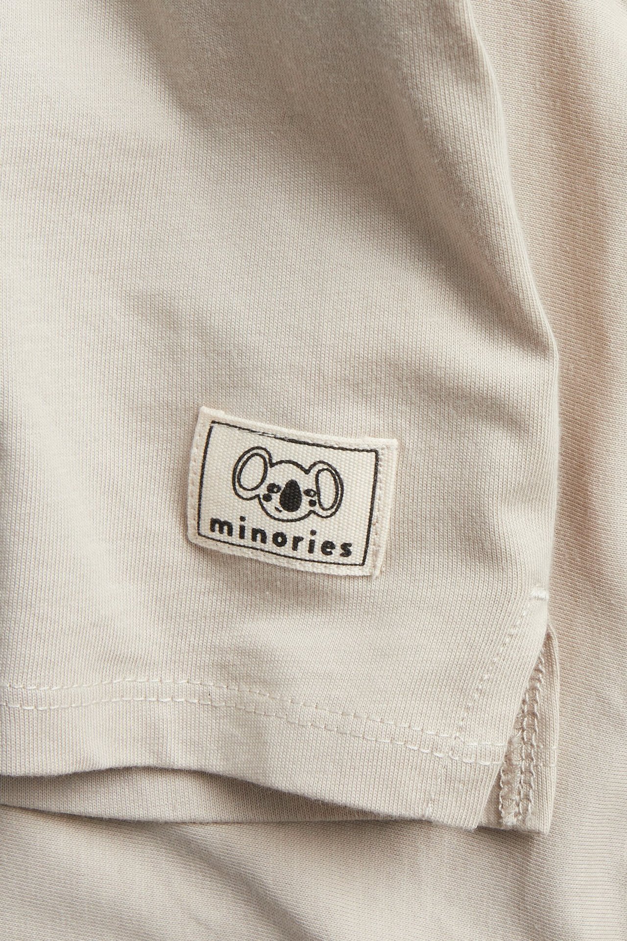 Zbliżenie: beżowa, bawełniana koszulka z długim rękawem z naszywką 'minories' koala.