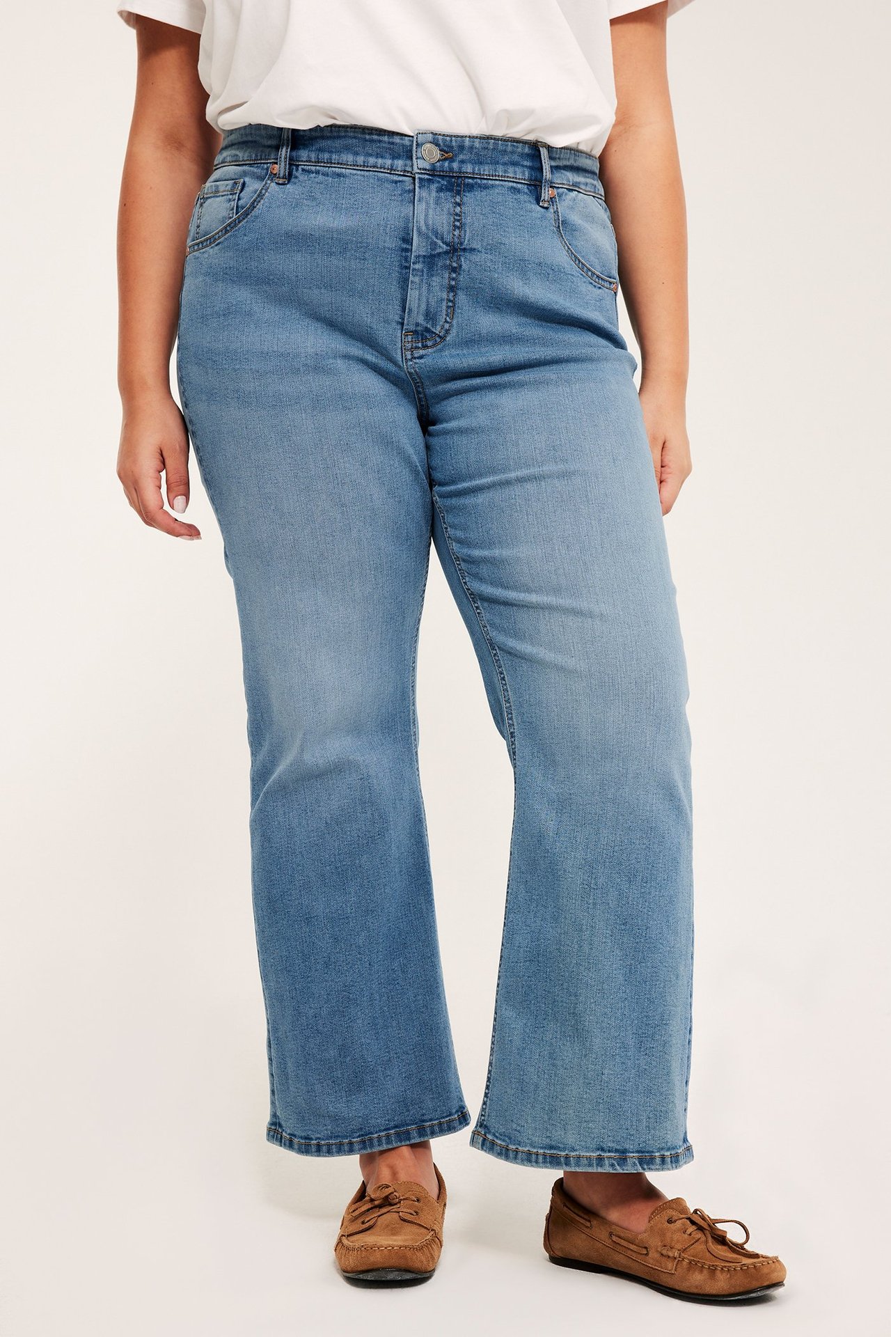 Frontvy av en kvinna i ljusblå högmidjade cropped flare-jeans med vit t-shirt och bruna mockasiner.