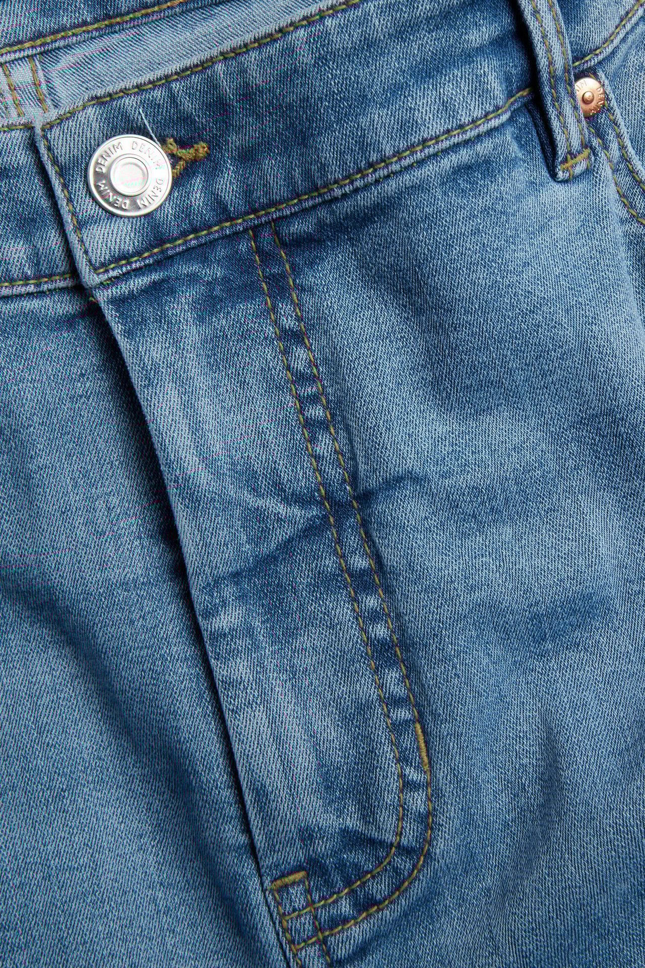 Zbliżenie na jasnoniebieskie jeansy z wysokim stanem, z denimu, ze srebrnym guzikiem i szwami.