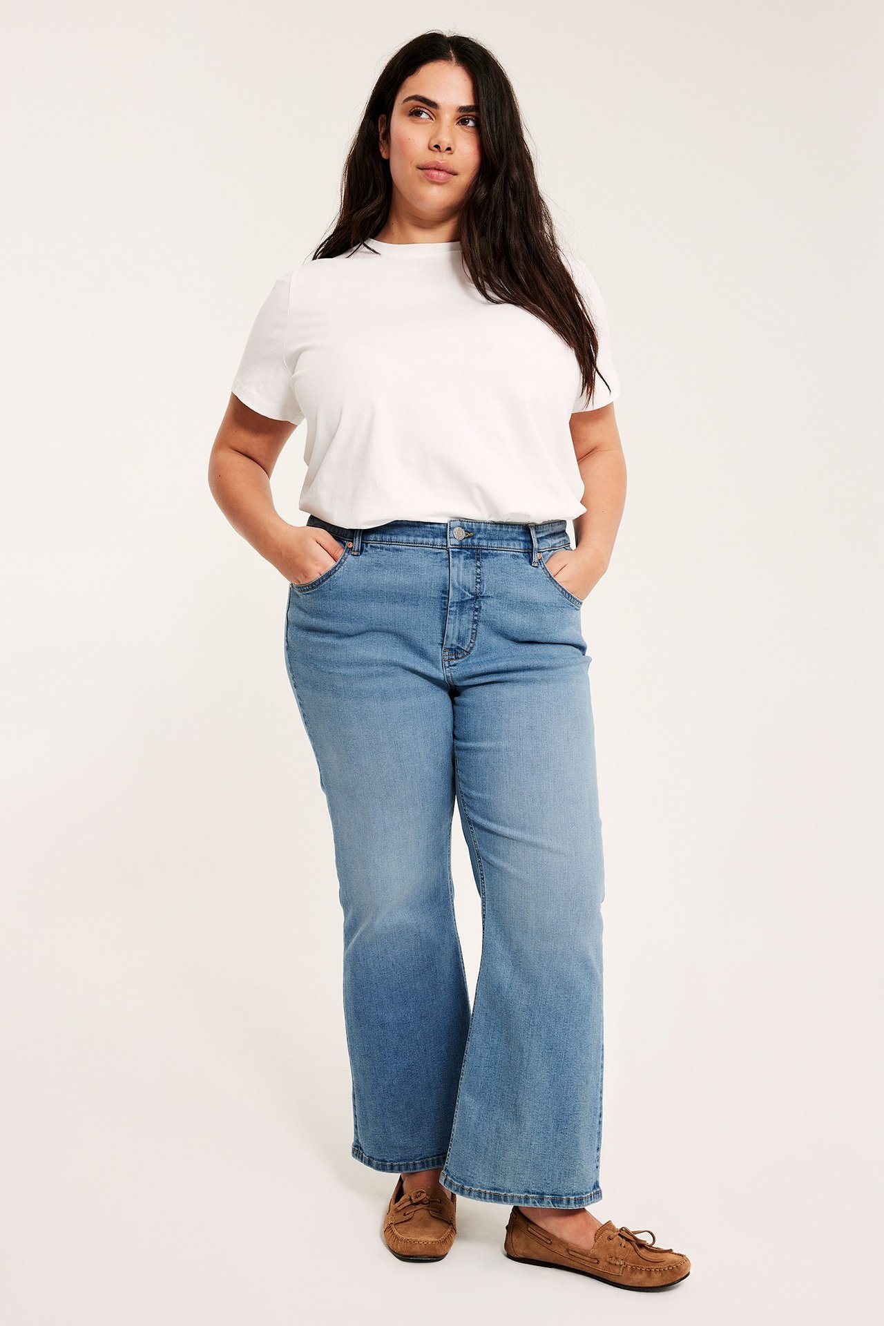 Frontvy av en kvinna i ljusa cropped flare-jeans med hög midja, vit t-shirt och bruna mockasiner.