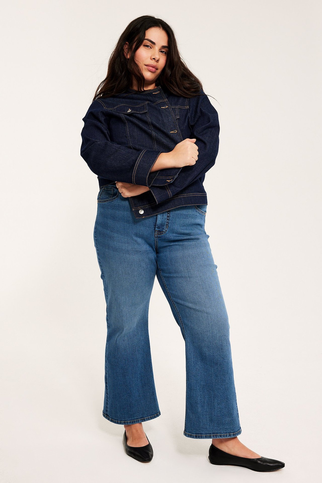 Widok z przodu: kobieta w niebieskich dżinsach flare, ciemnogranatowej kurtce dżinsowej i czarnych butach.