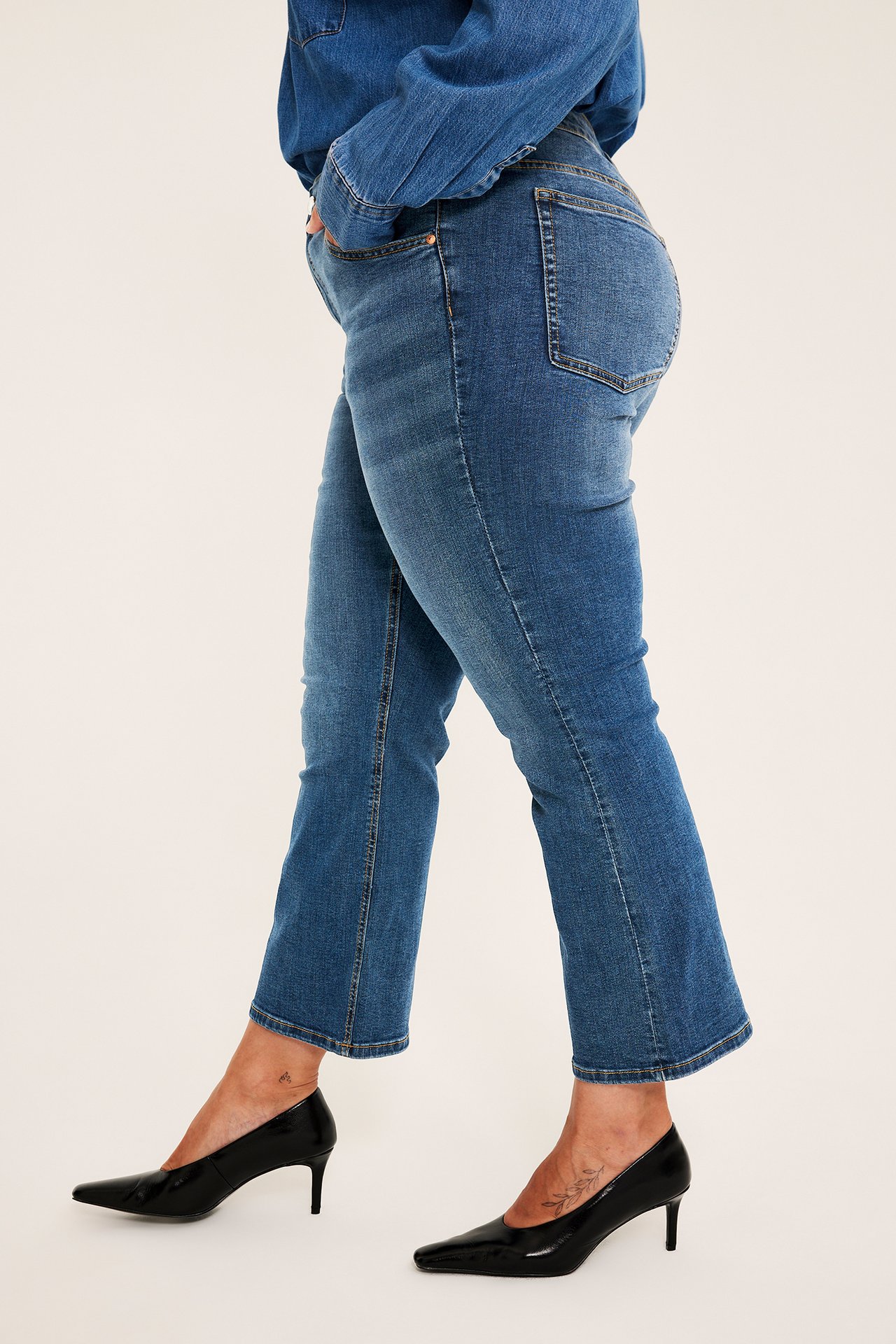 Sidovy av en kvinnlig modell som bär blå denim croppade flare-jeans och svarta spetsiga klackar.