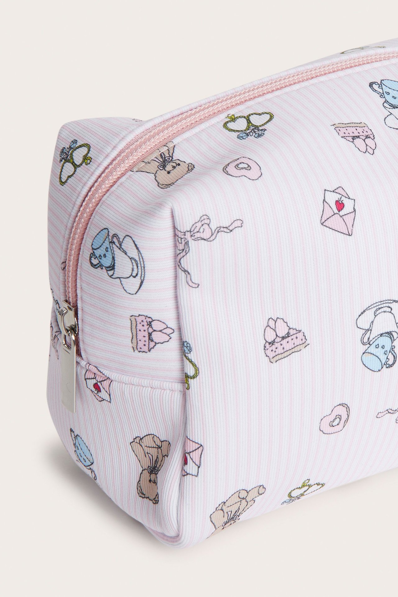 Lähikuva off-white kuvioidusta toilettilaukusta ohuilla vaaleanpunaisilla raidoilla ja vetoketjulla.