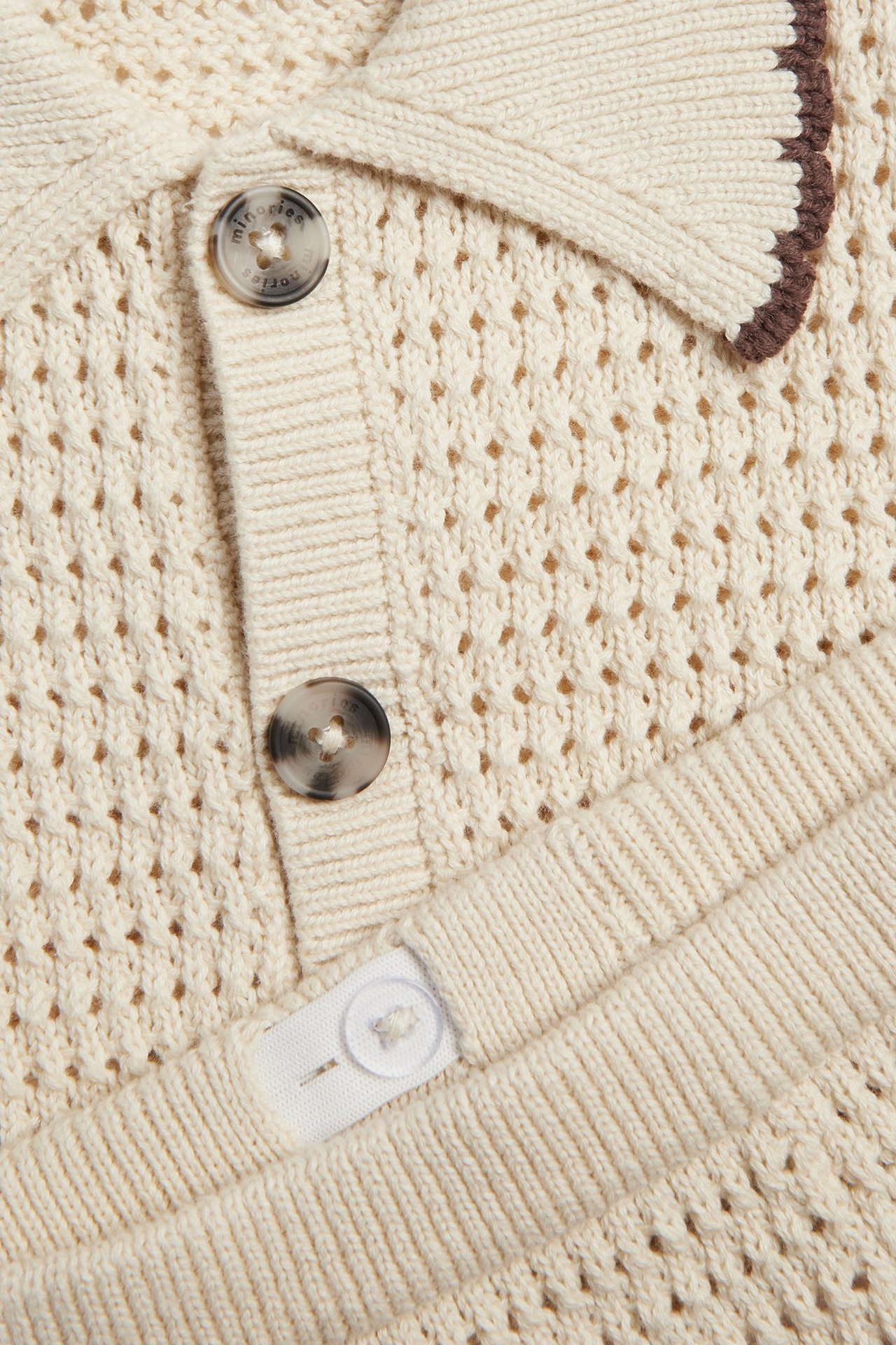 Zbliżenie na beżowy, dziergany komplet dziecięcy: koszulka z kołnierzykiem i guzikami oraz szorty z regulowaną talią.