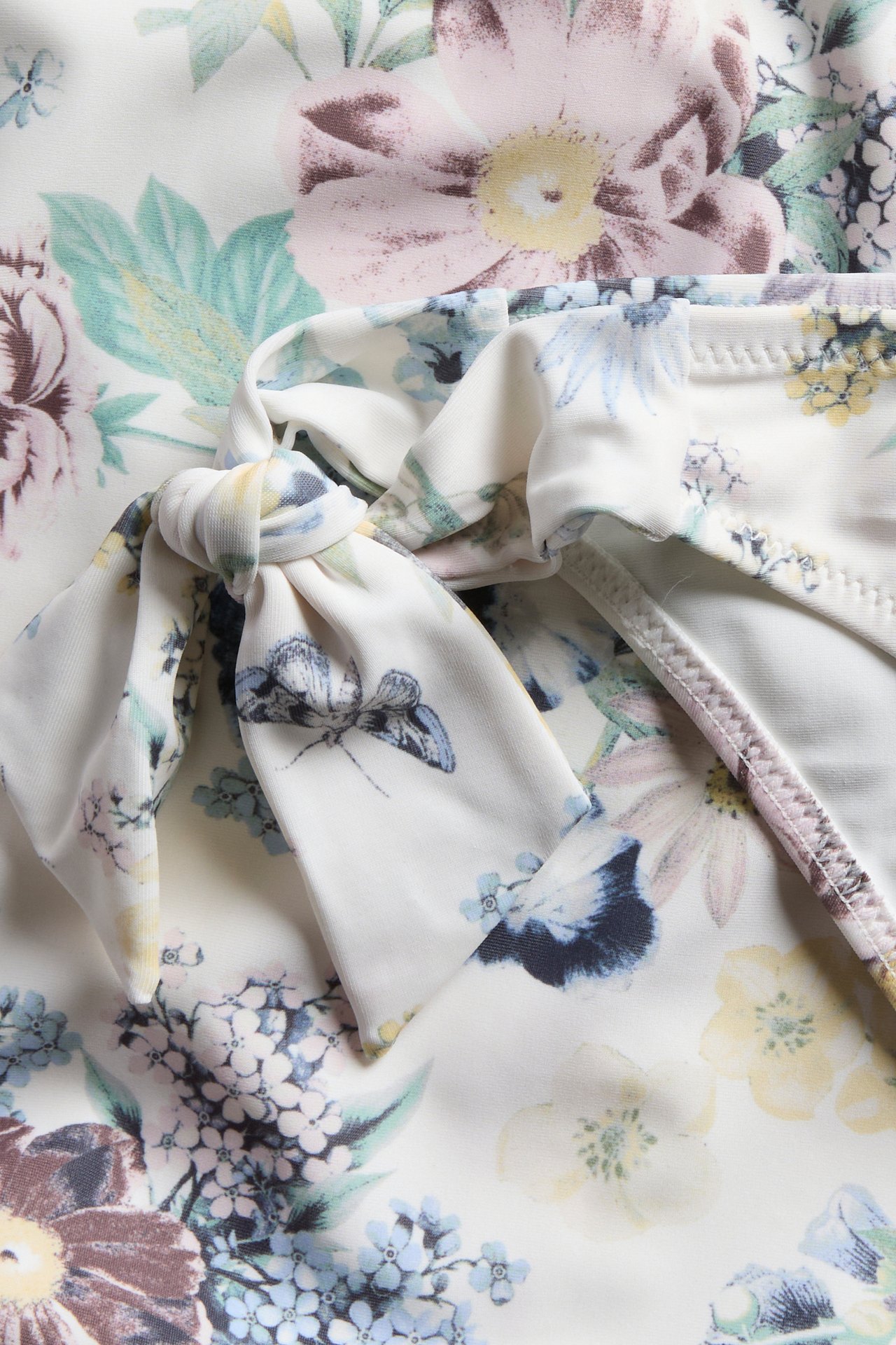 Närbild av offwhite blommig brazilian bikinitrosa, med knytband och fjärilsdetalj på blommönstret.